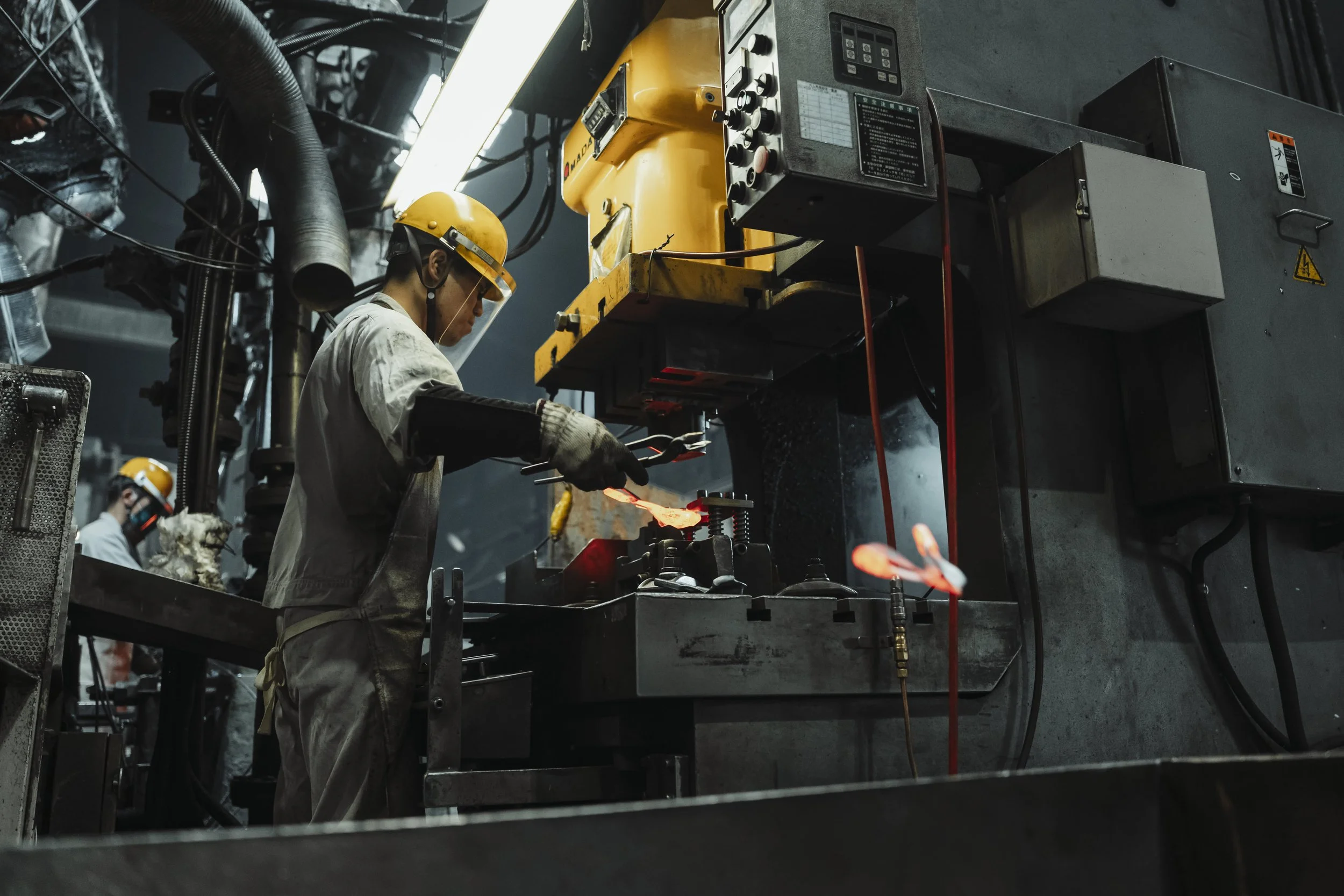 A worker in safety gear operating a metal pressing machine in a factory.
