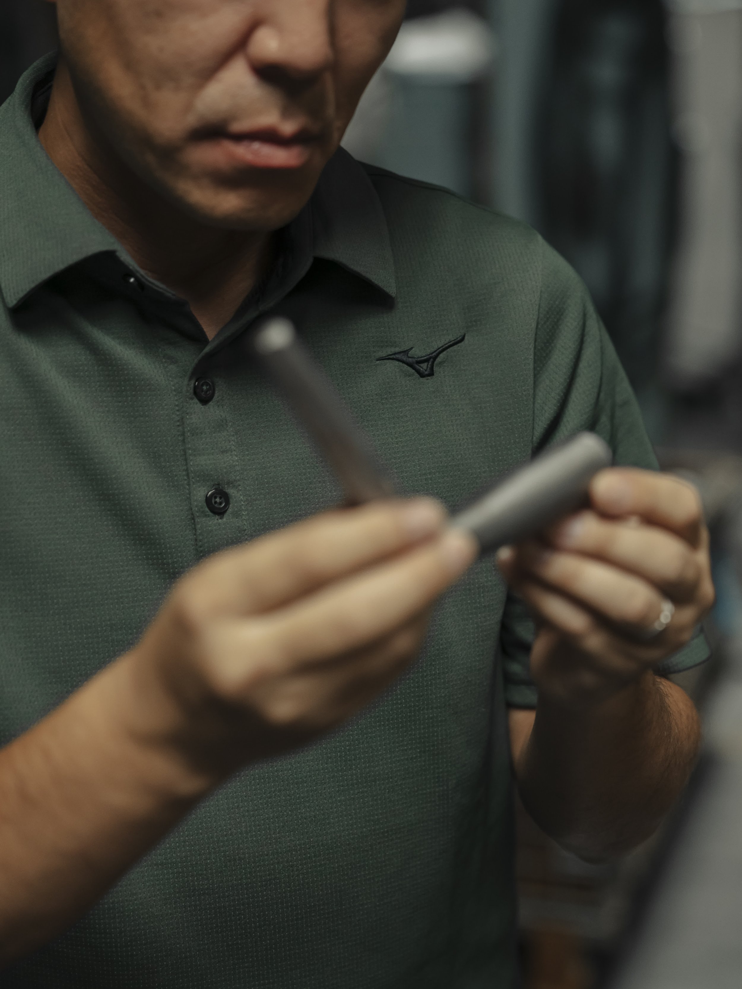 A man wearing a green shirt is looking at his smartphone while holding a stylus pen.