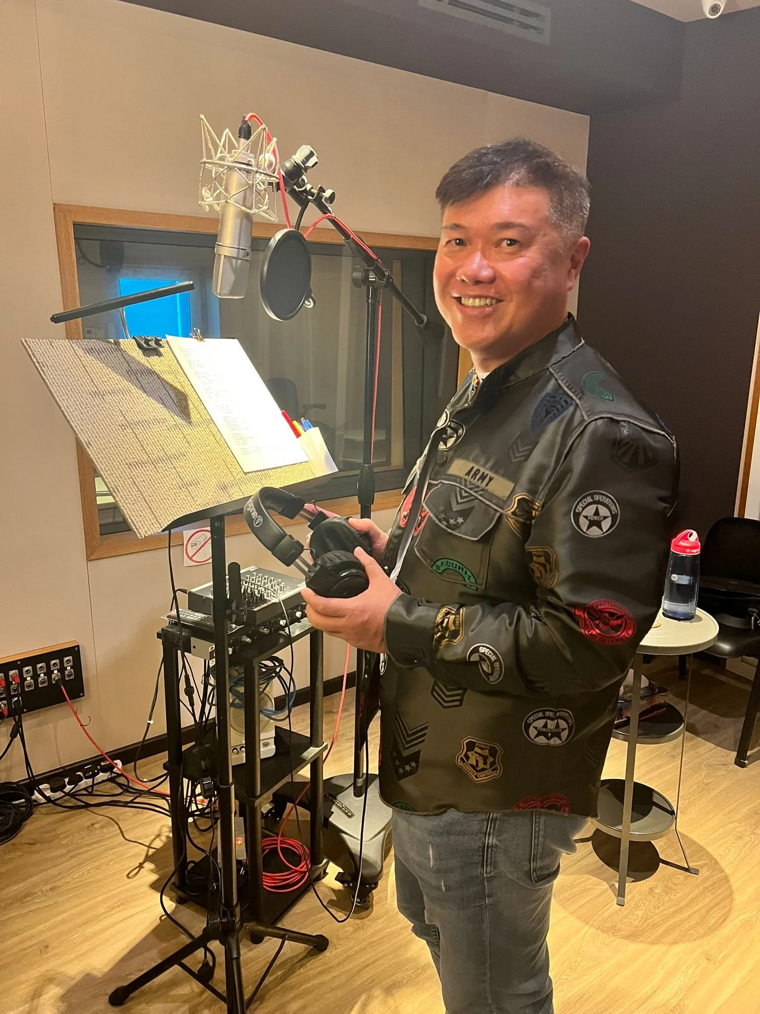 Person in recording studio holding headphones, with microphone and music stand.