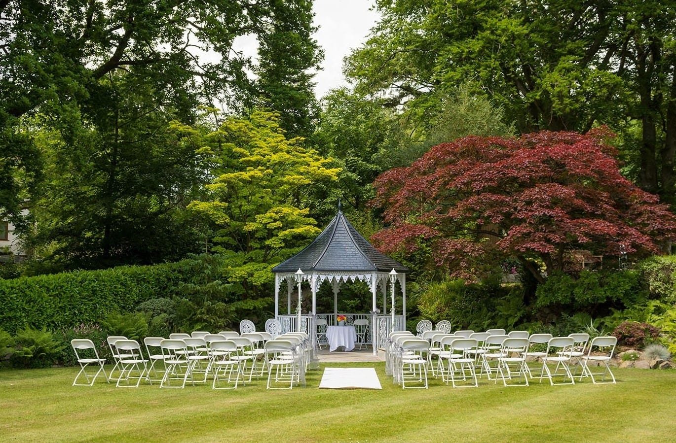 Outdoor wedding setup with a gazebo surrounded by chairs and trees.