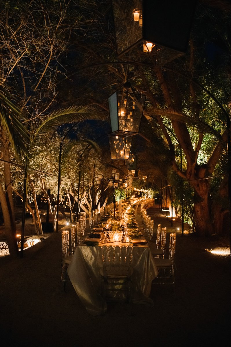 Outdoor dinner setup under lantern lights at night, surrounded by trees.