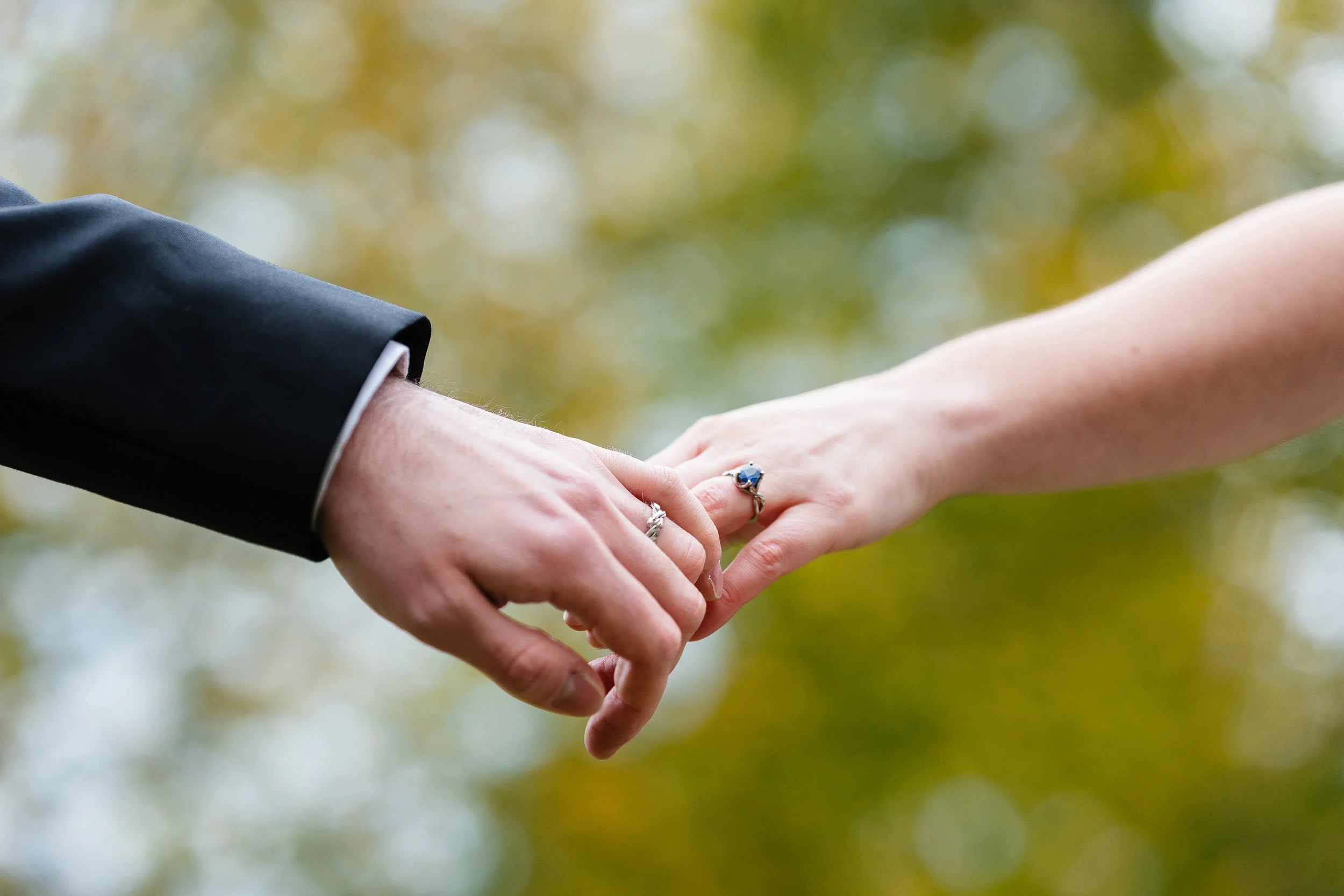 Bride and Groom hands and rings pictured with fall colored trees in the background at Schuylkill River Park in Philadelphia, PA. 