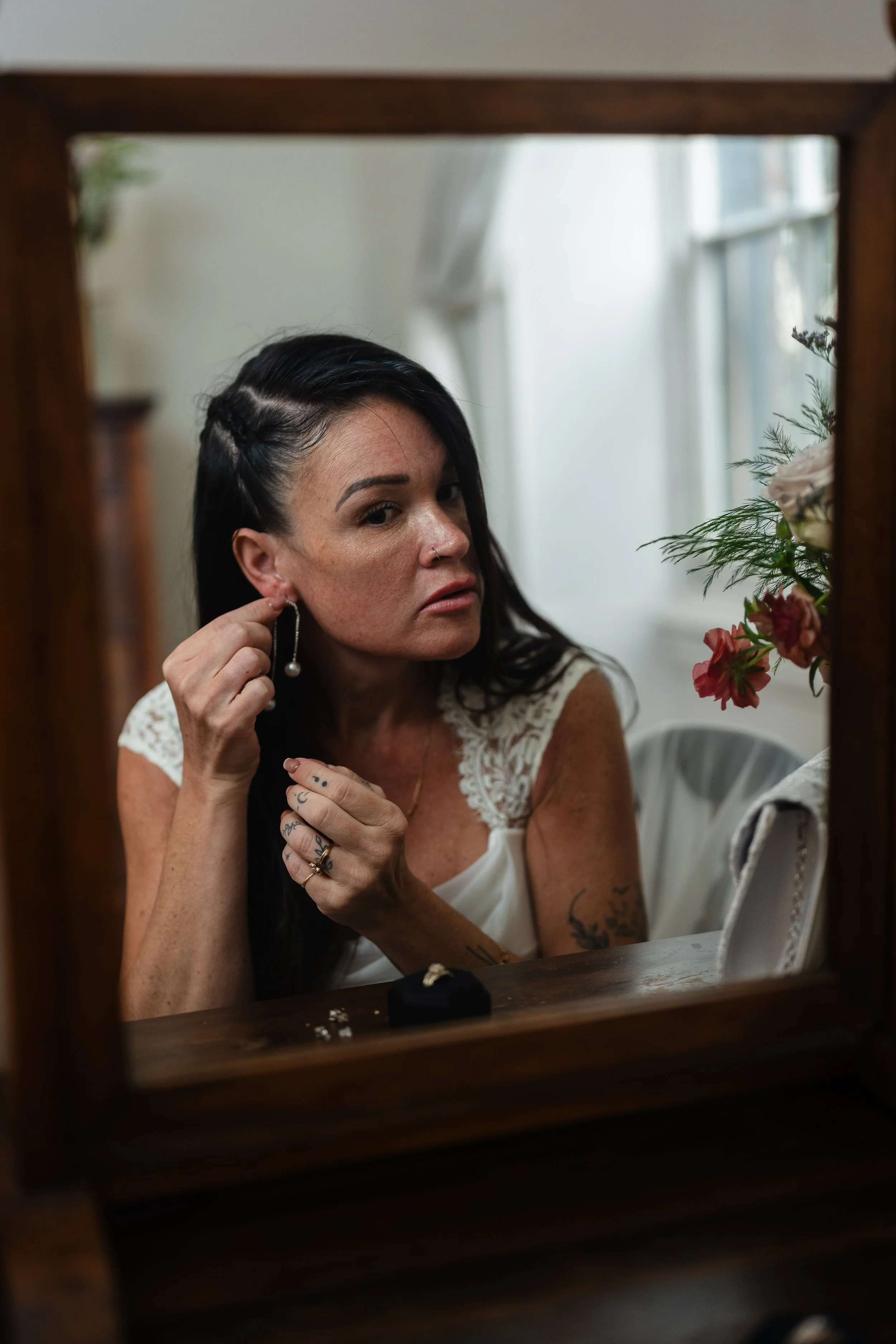 Brides reflected in mirror while putting on earrings at Vaux Studios in Philadelphia, PA. 
