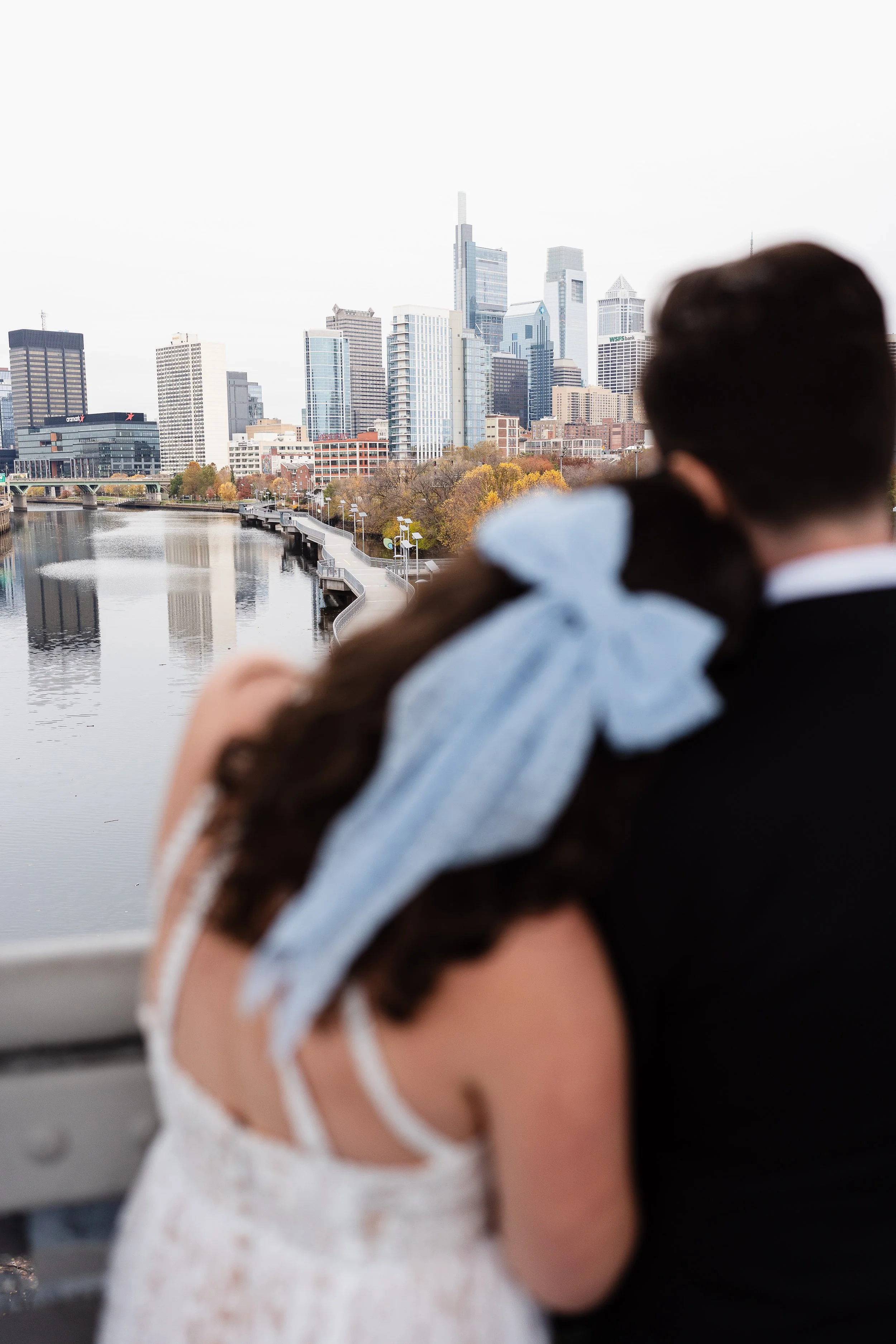 Bride laying head on grooms shoulder while looking out to the Philadelphia city scape. 