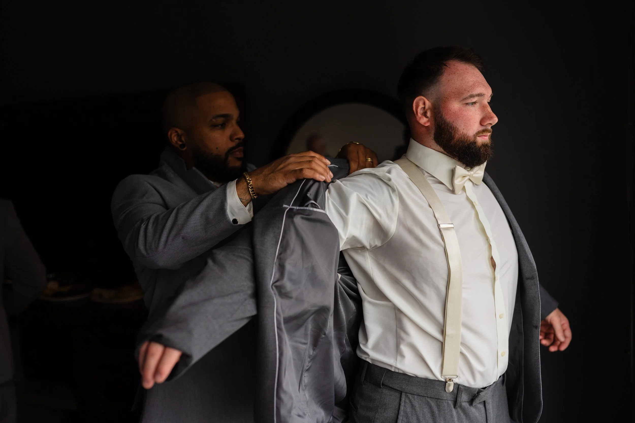 Best man helping groom put jacket on during groom prep photos at Holiday Inn in Deptford New Jersey