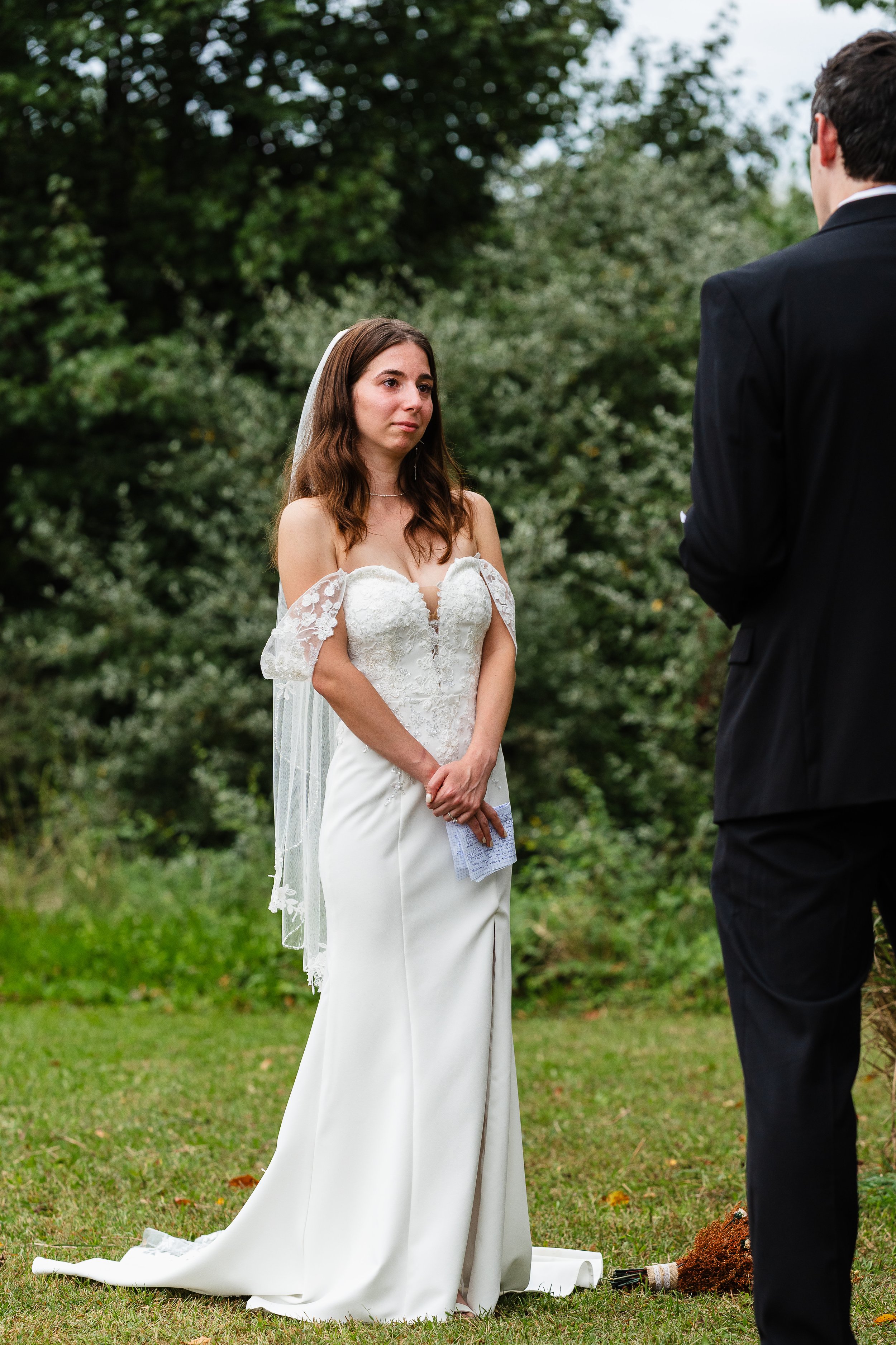 Bride emotional during ceremony as she listens to vows, backyard wedding in Newfield, New Jersey. 