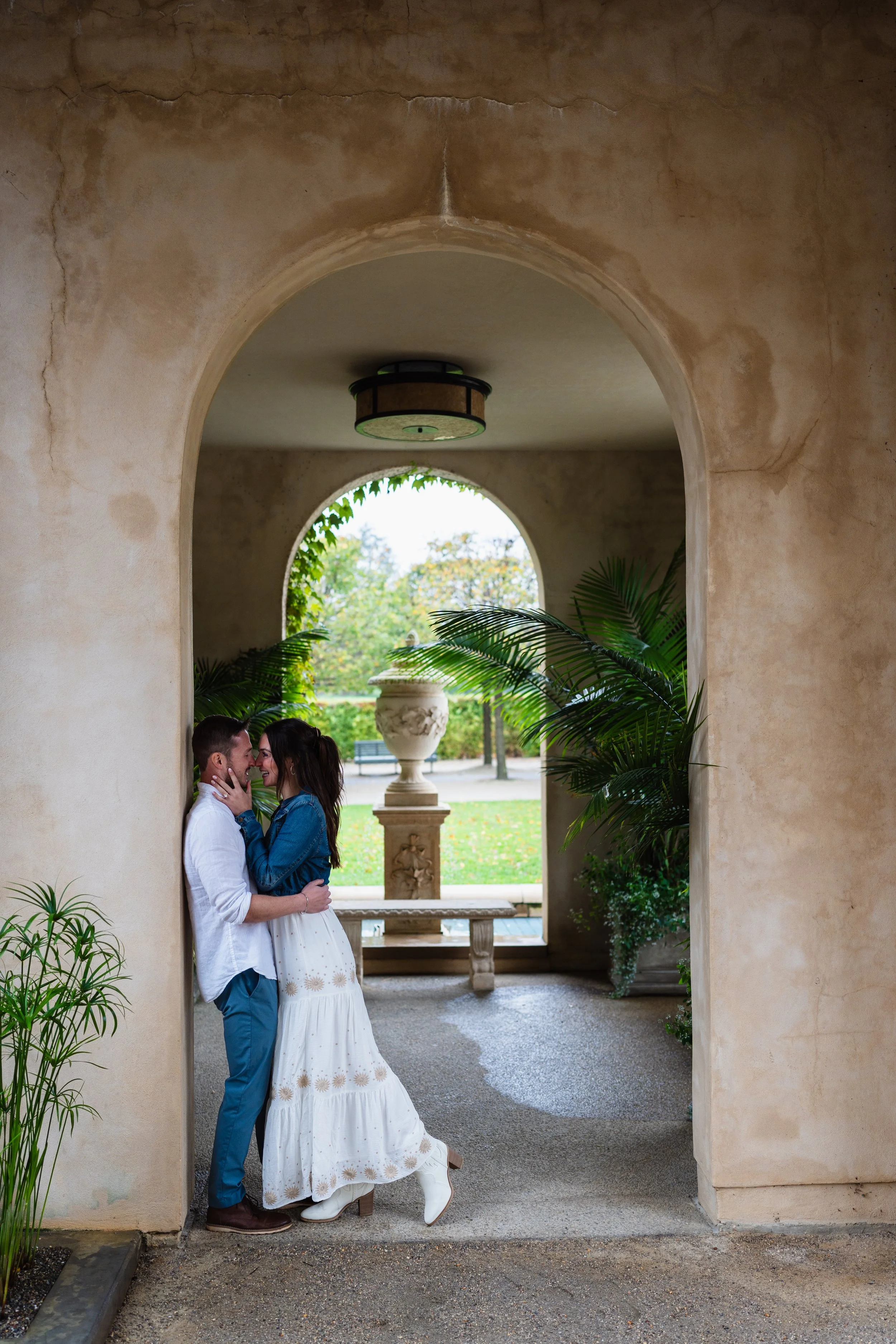 Couple embracing while framed by archway ay Longwood Gardens during their engagement session.