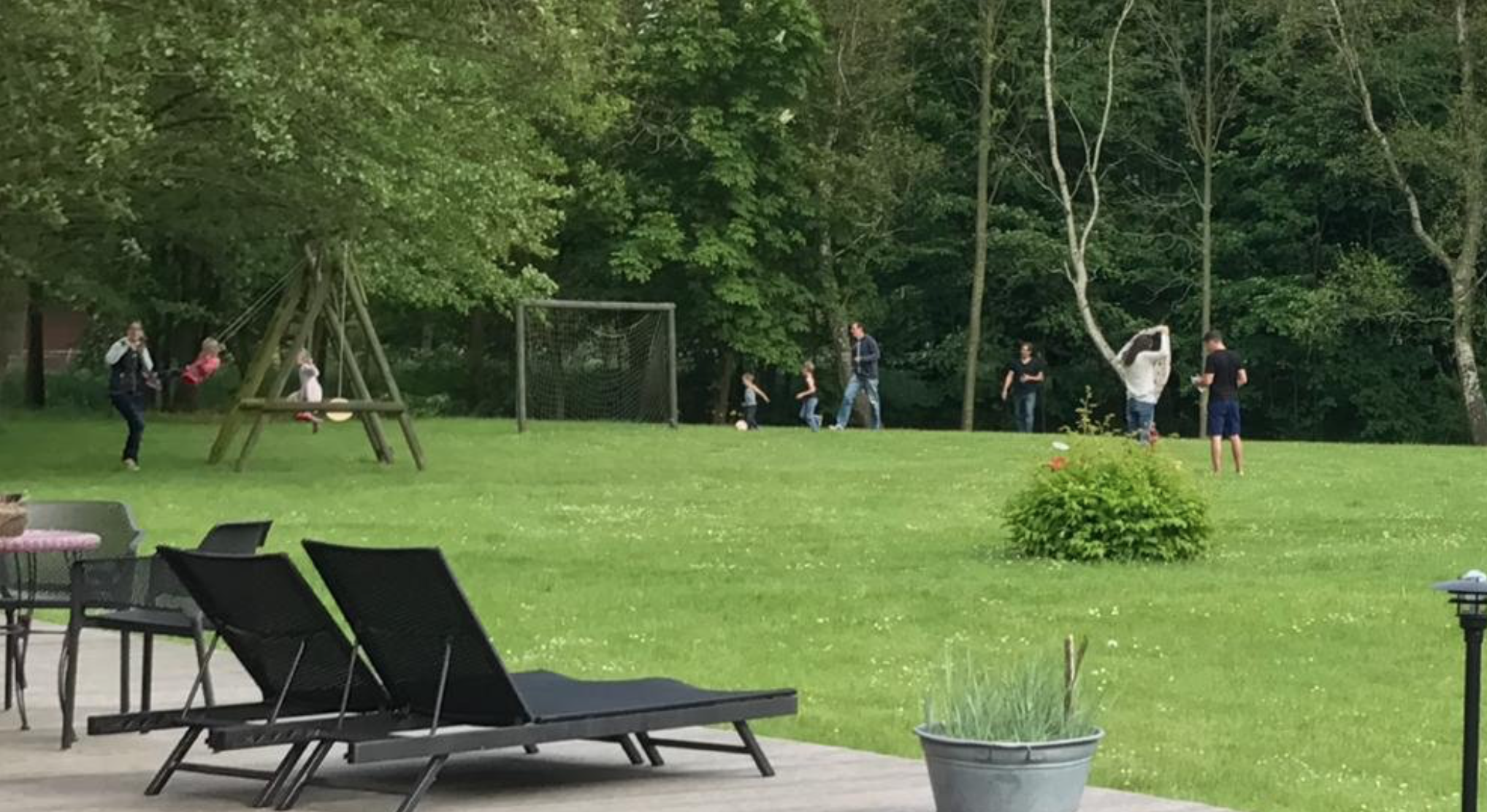 Familie und Kinder spielen im Park, während auf der Terrasse Liegen und Gartenmöbel stehen im Tümlauer Koog auf Ferienhof Hartwig.