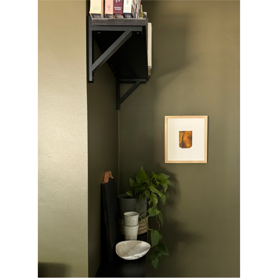 small framed brown artwork shown against a dark green wall in stylish room
