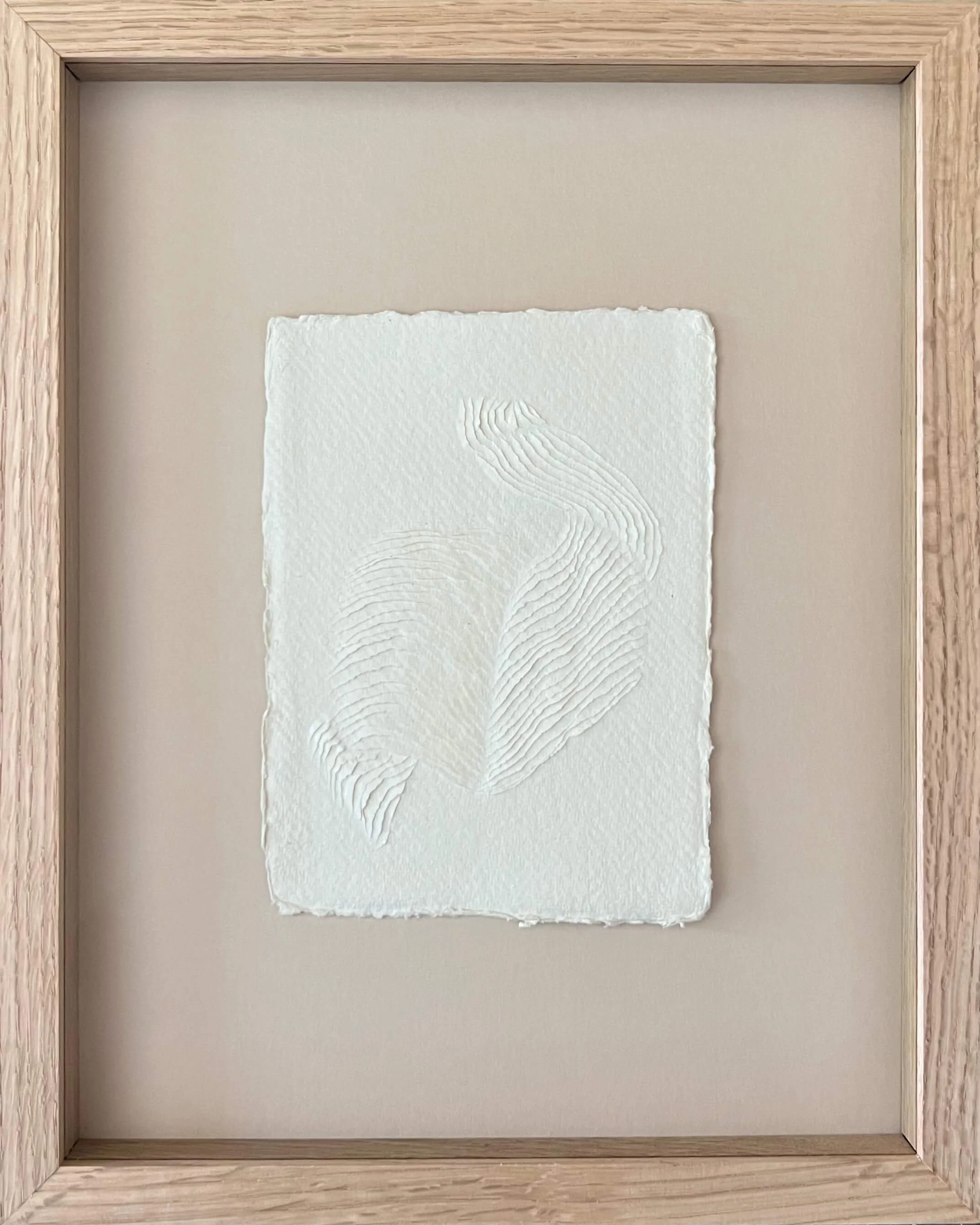 small all white artwork with a 3D textured surface that's carved into the surface creating an image flowing across the paper. Framed in oak with artless