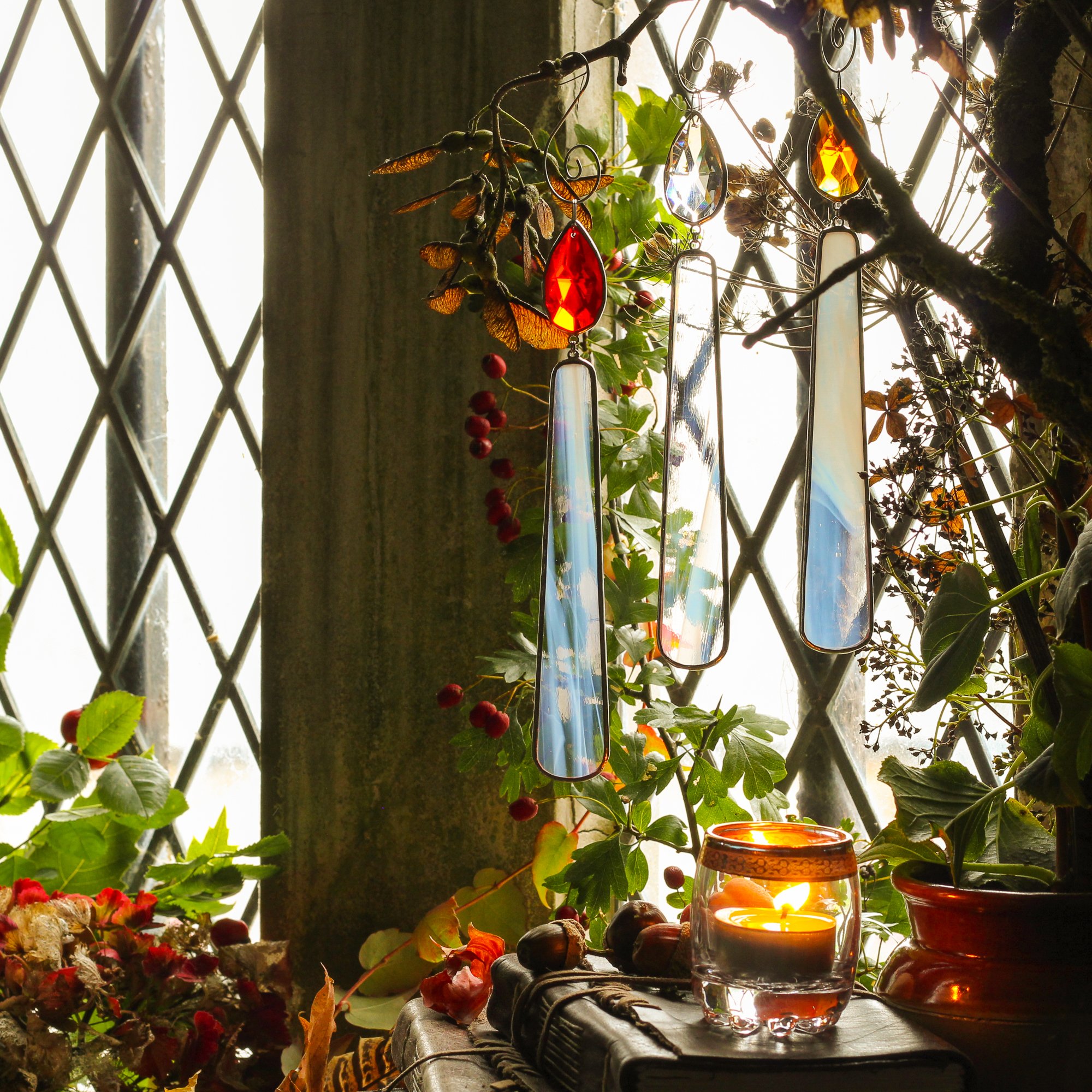 Autumnal lifestyle shot showing three stained glass candles with crystal flames hanging in front of a traditional leaded light window. Witchcore.