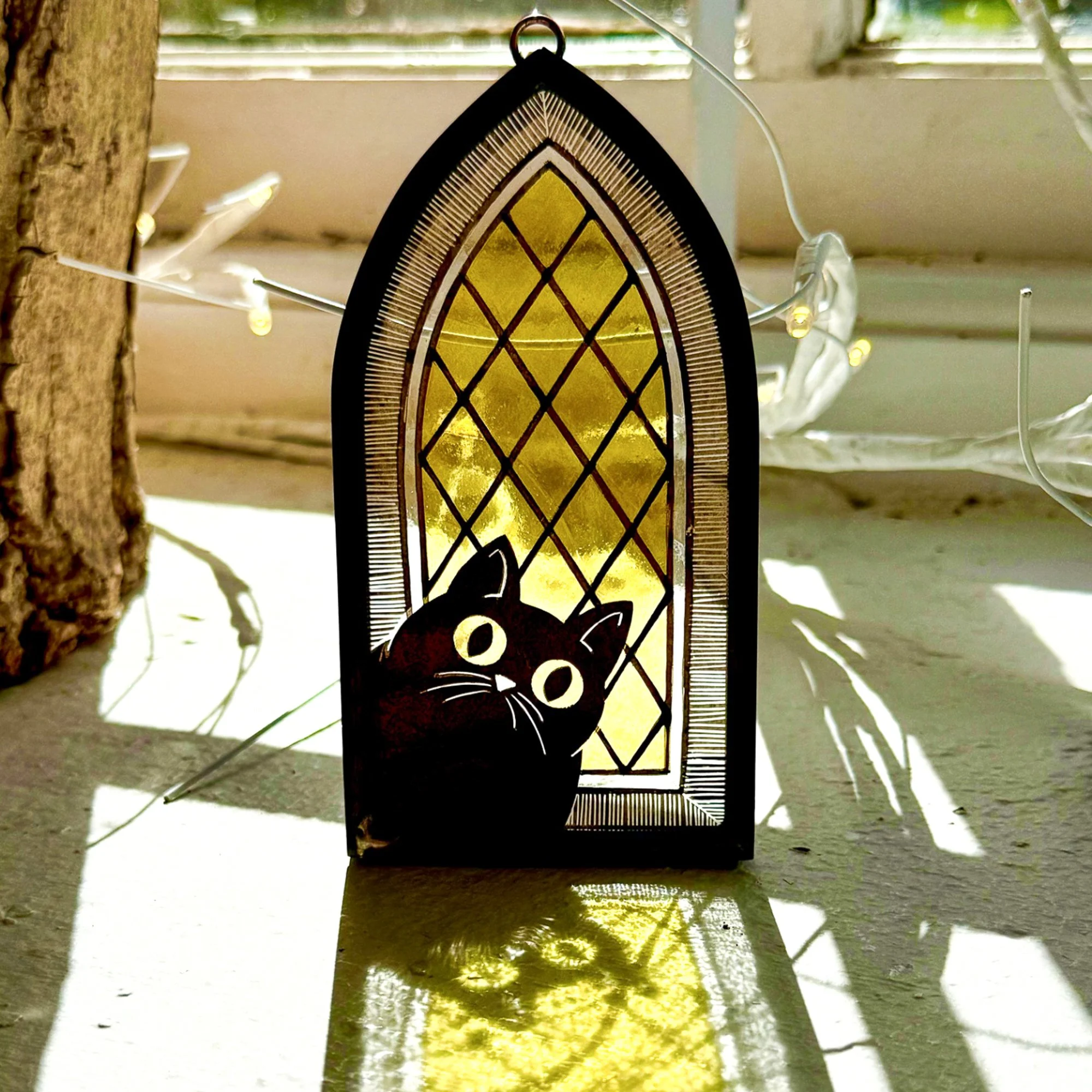 Traditional hand painted stained glass cat with lead surround. The cat is silhouetted against a traditional quarry design stained glass window. Ann Smyth Stained Glass