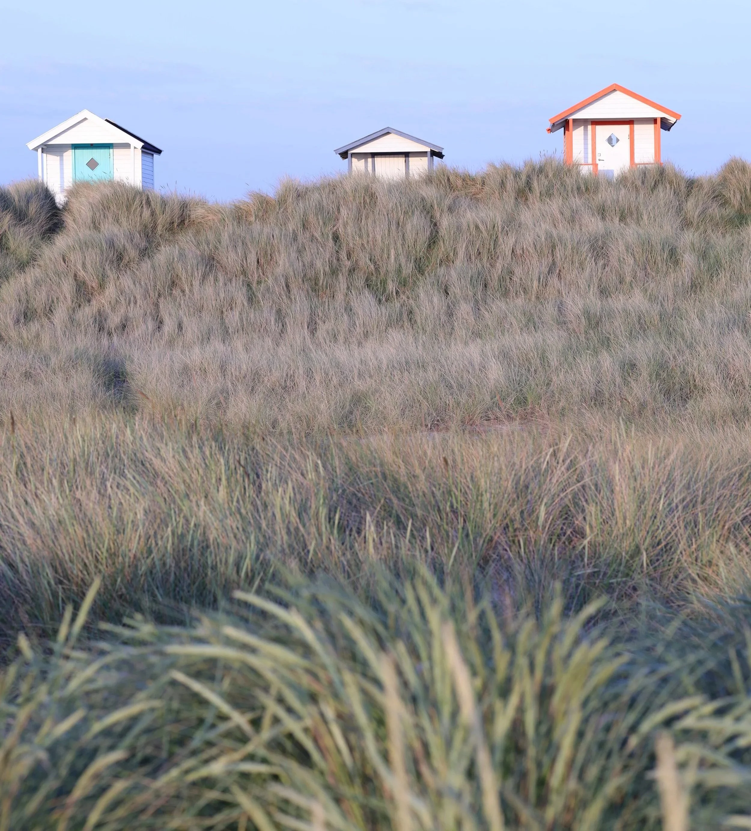 Tre små sommarstugor på en sanddyn täckt av gräs.
