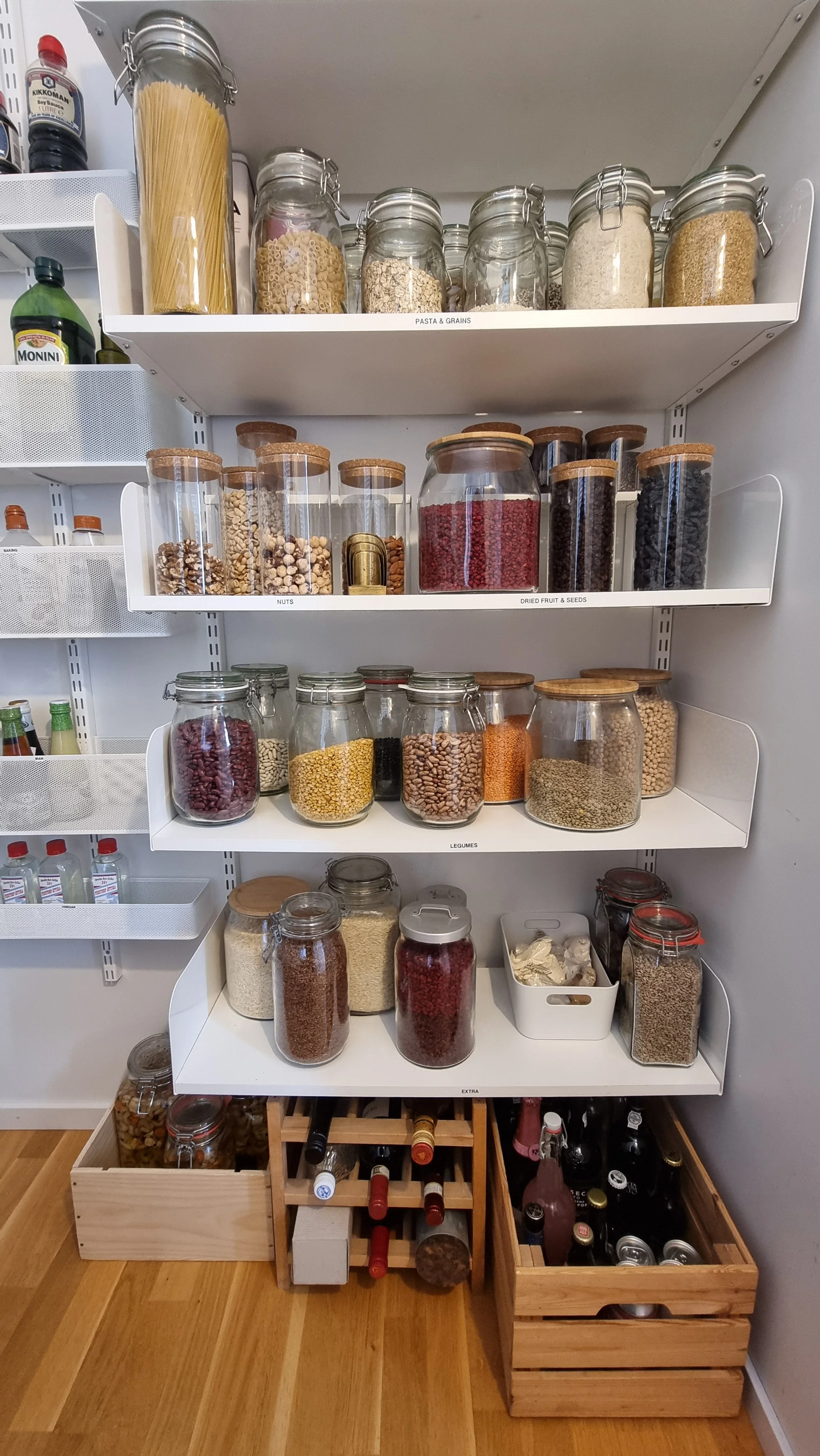 Bild av ett skafferi med olika burkar och lådor fyllda med pasta, frukt, nötter, grönsaker, ris och andra torra livsmedel.