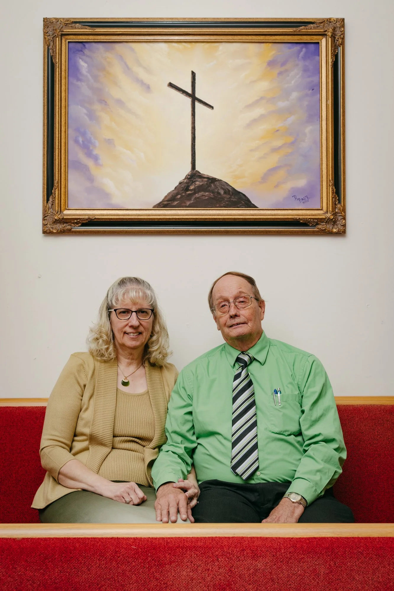 Karen and Jerry Holden pose for a portrait under a painting of a cross at Merry Oaks Baptist Church in Chatham County, N.C. on Oct. 30, 2022. The two met at the church when they were mere children, and consider it a second home. Now, an impending mul