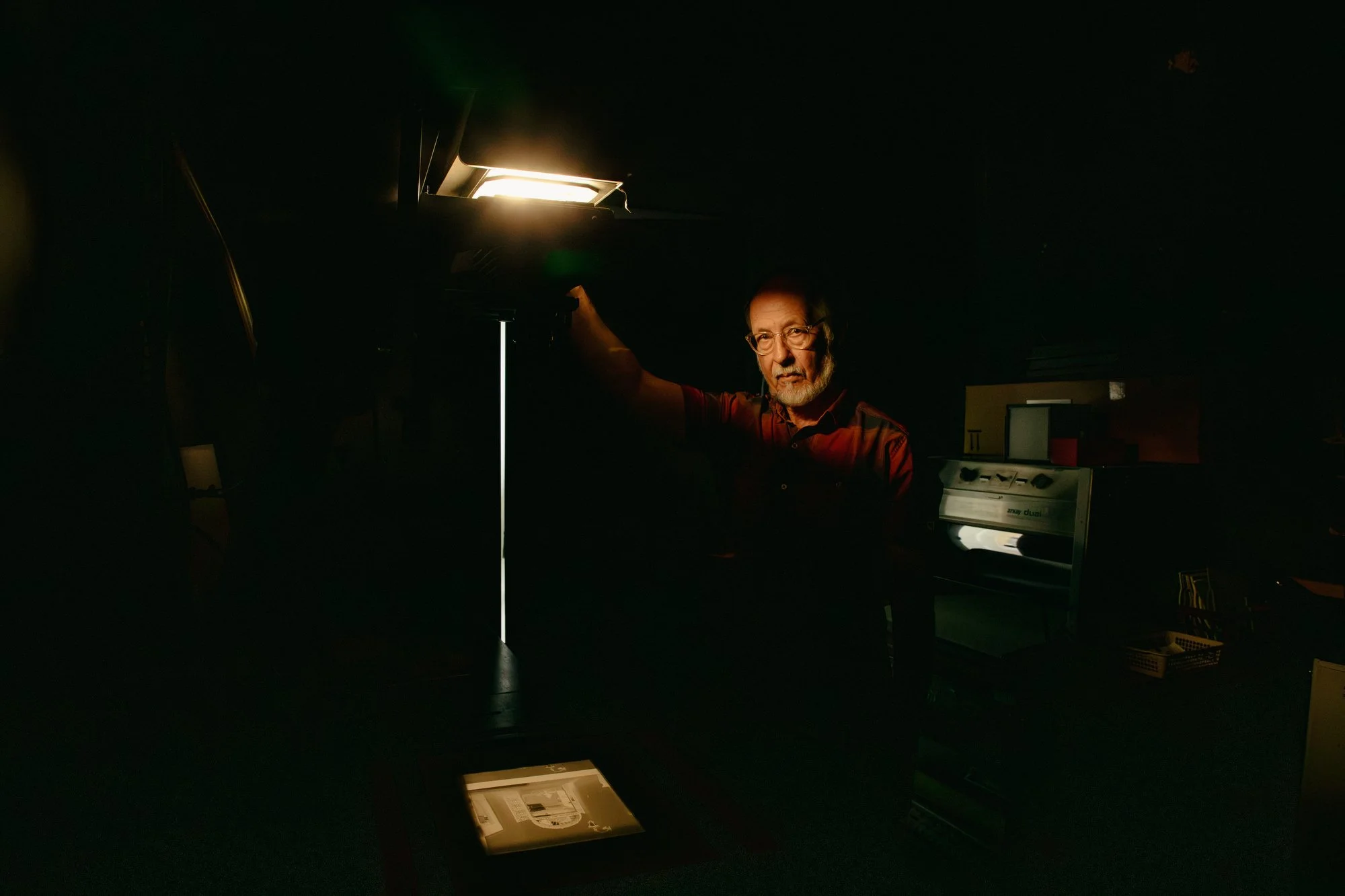 Bill Wierzalis, analog film photographer, poses for a portrait at Full Circle Fine Arts in Baltimore, Md. on July 11, 2022. This portrait was made using solely available light from the enlarger.