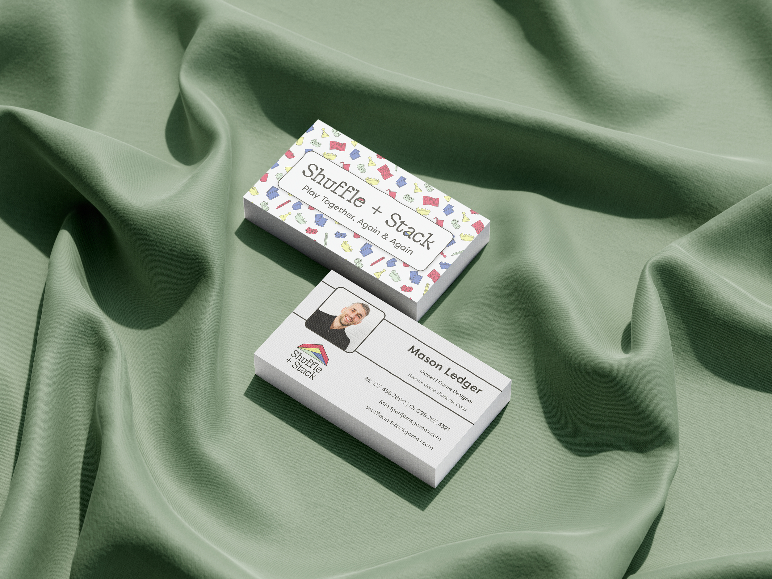 A business card for Mason Ledger from Shuffie + Stack, resting on light green fabric. The card displays his picture, name, contact details, and a logo with colorful puzzle piece icons.
