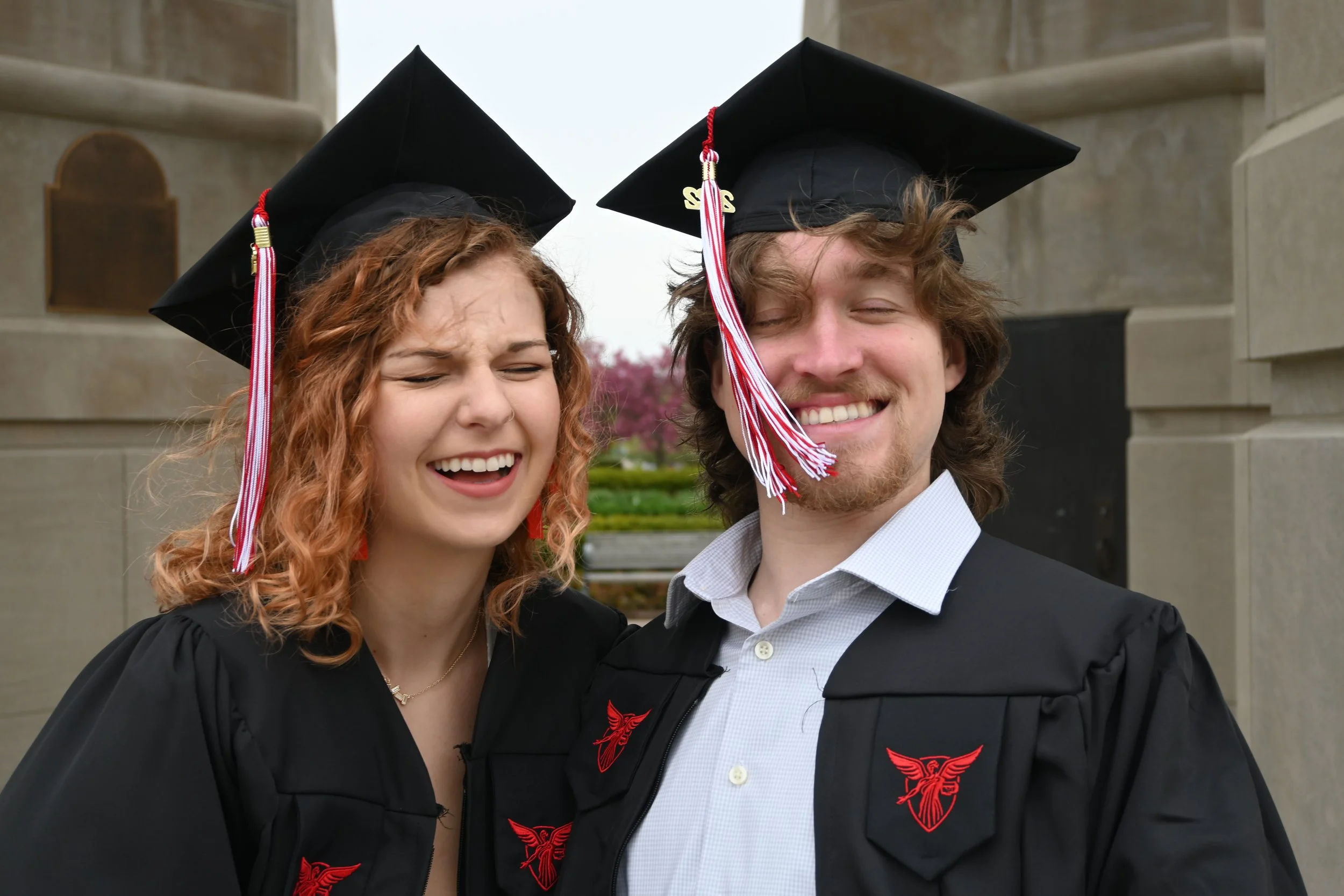 Two graduates in caps and gowns smiling for a photo outdoors.