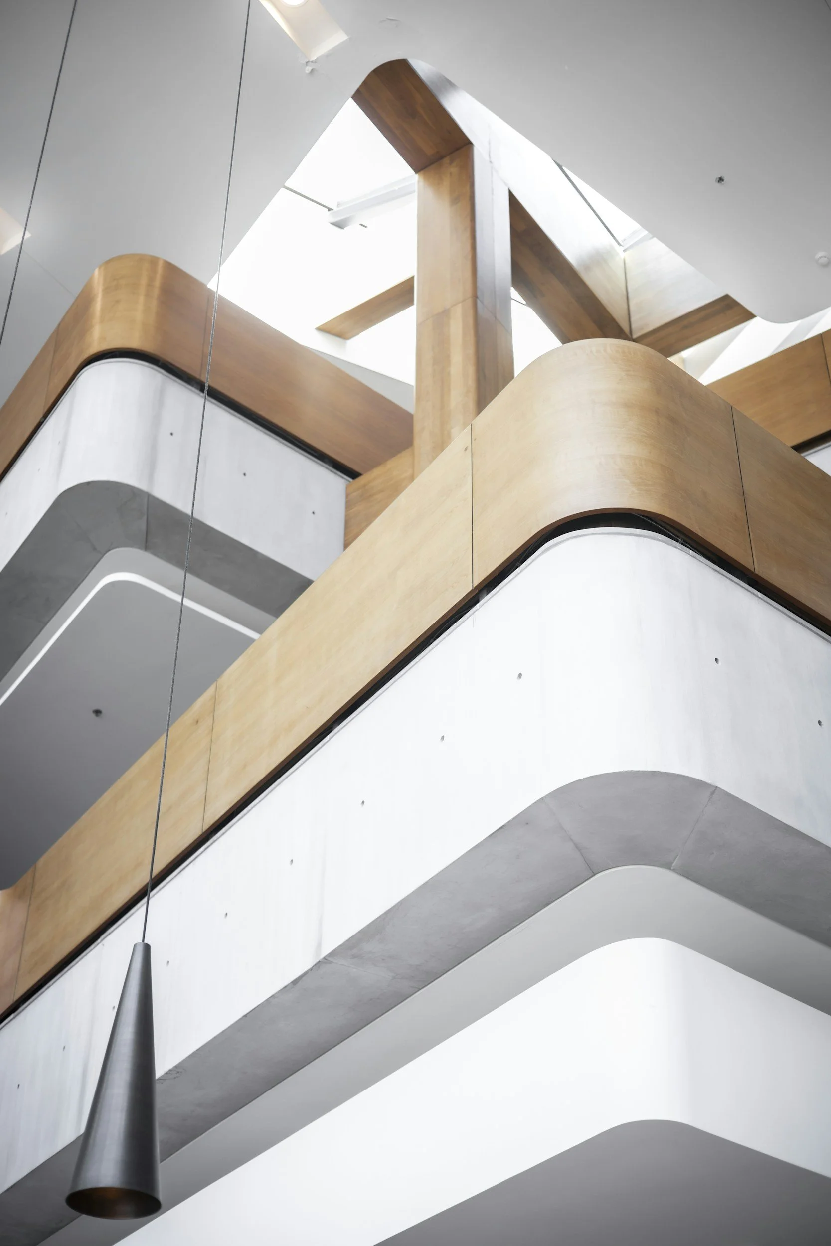 Interior view of a modern building with balconies featuring wood paneling and a white concrete ceiling and walls, viewed from below.