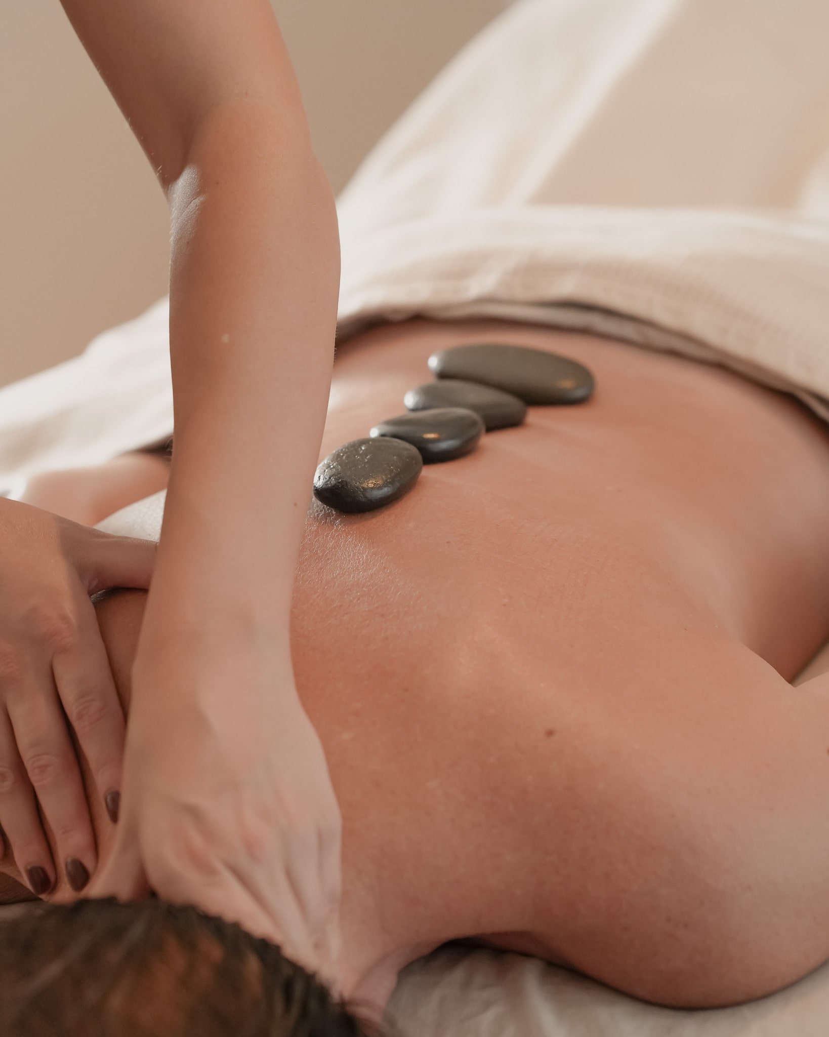 A person receiving a hot stone massage on their back, with smooth black stones placed along their spine.