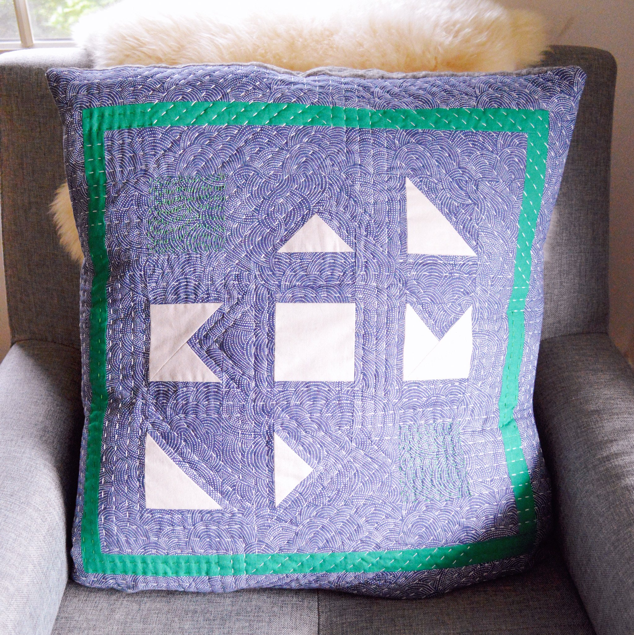  a hand quilted pillow that is blue with white geometric shapes and a green border 