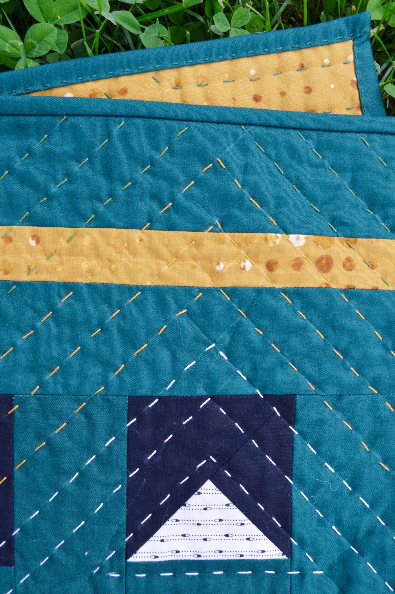  close-up of a hand-quilted wall hanging, the stitches are in white, yellow and green thread 