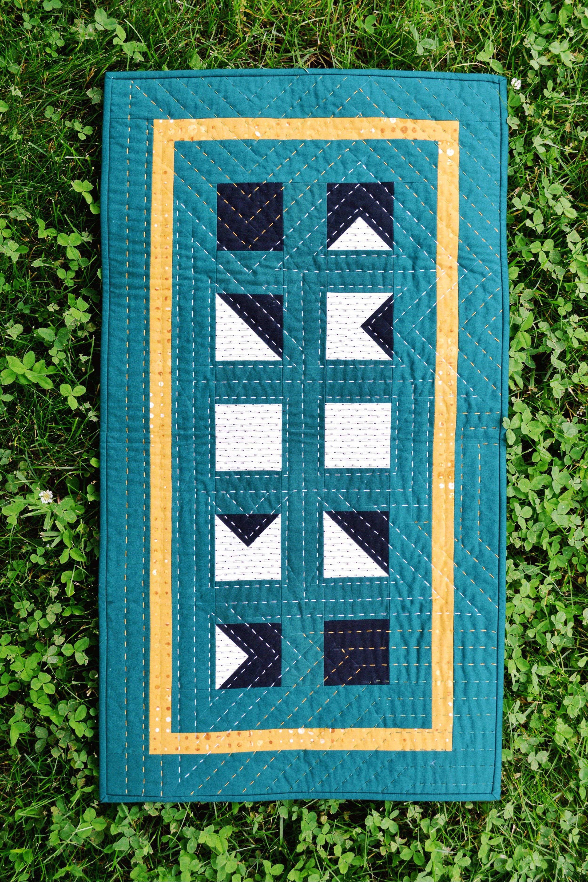 a green hand quilted wall hanging lying in a bed of green clover 