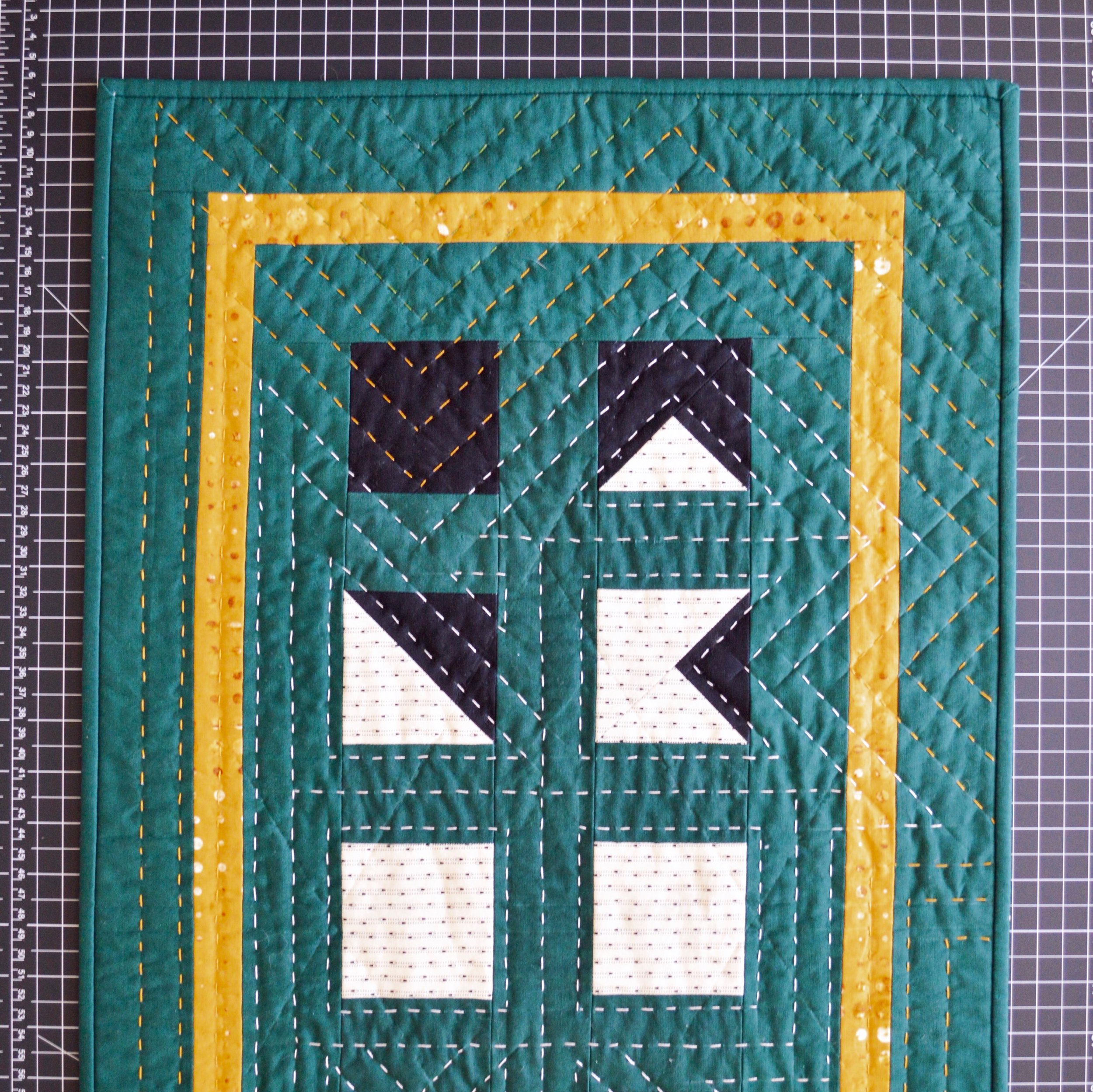  a green, hand-quilted wall hanging laying on a black cutting mat 