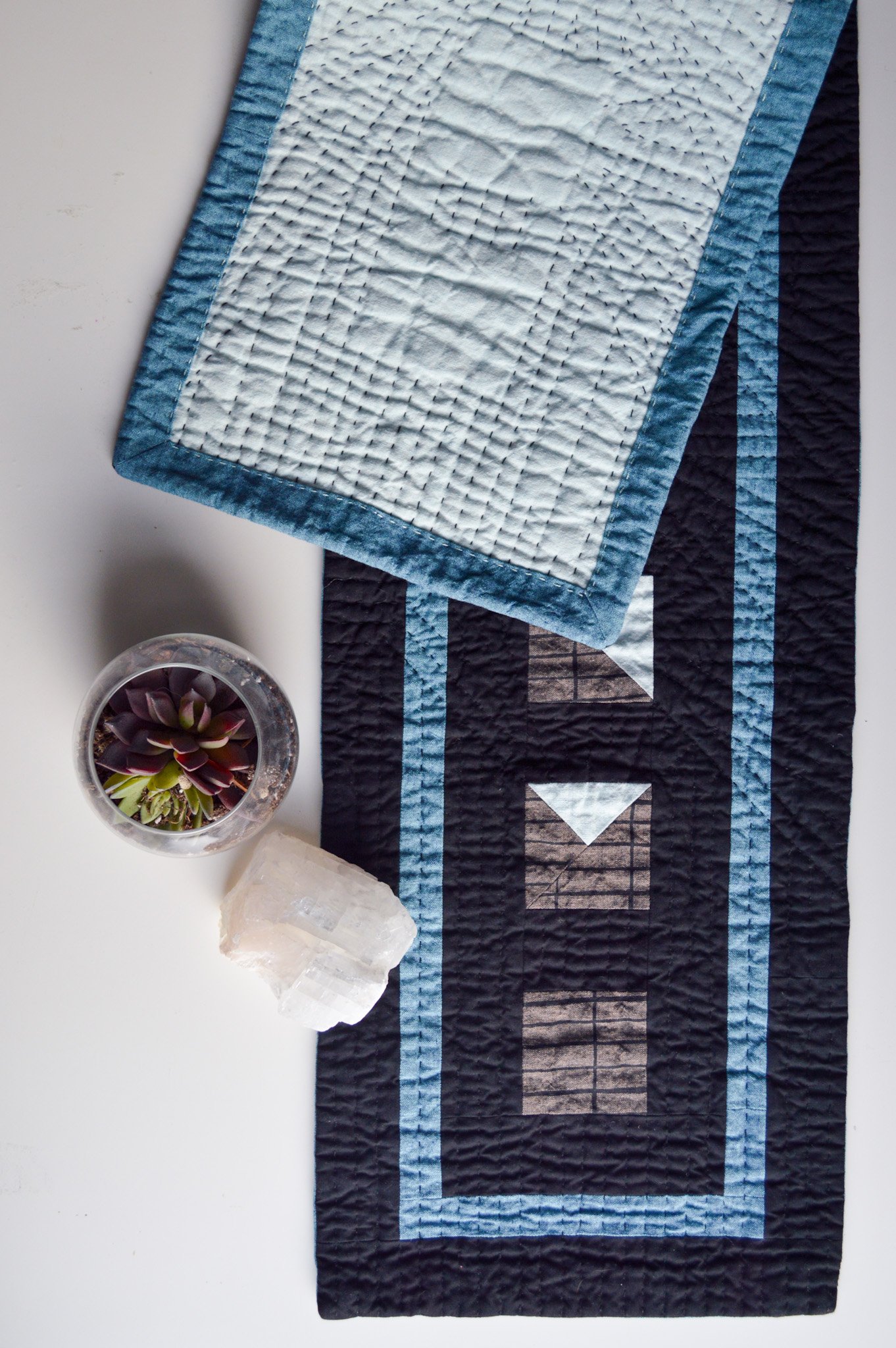  a hand quilted table runner that is black with brown and white half-square triangles and a blue border 