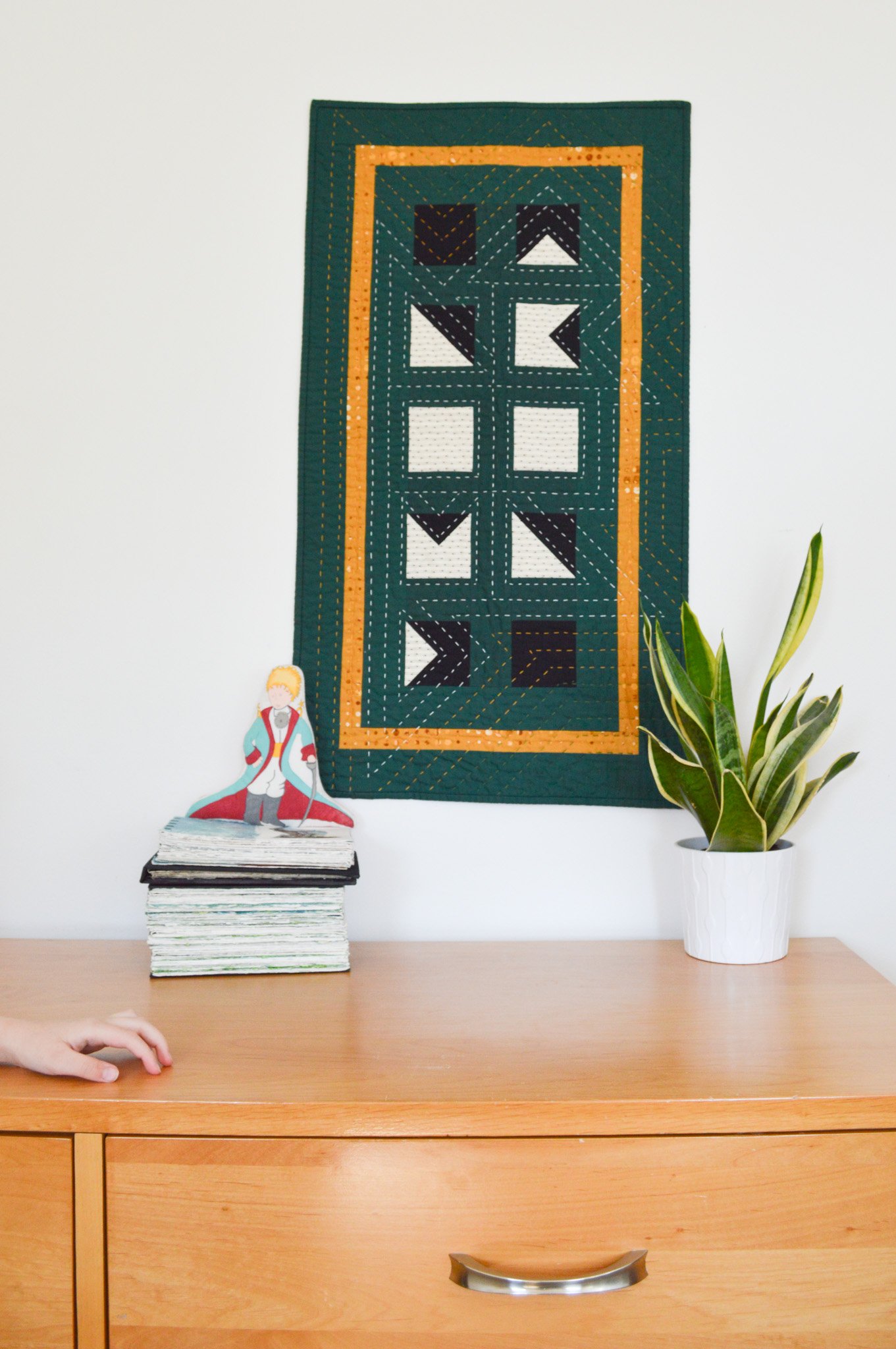  A green wall haning that is hand-quilted hanging above a modern style dresser  