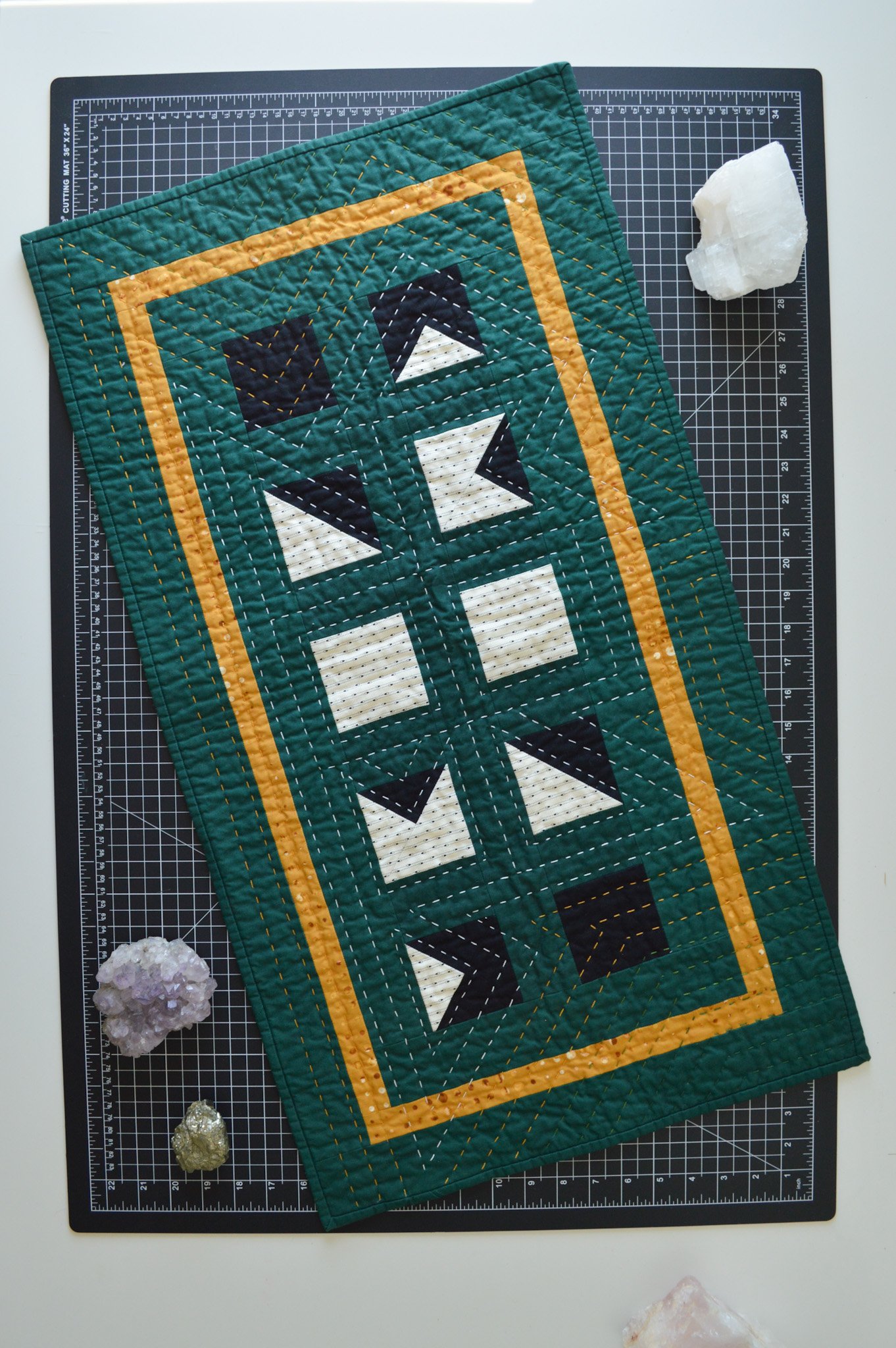  green, hand-quilted mini quilt on a black cutting mat with amethyst, pyrite and calcite stones 