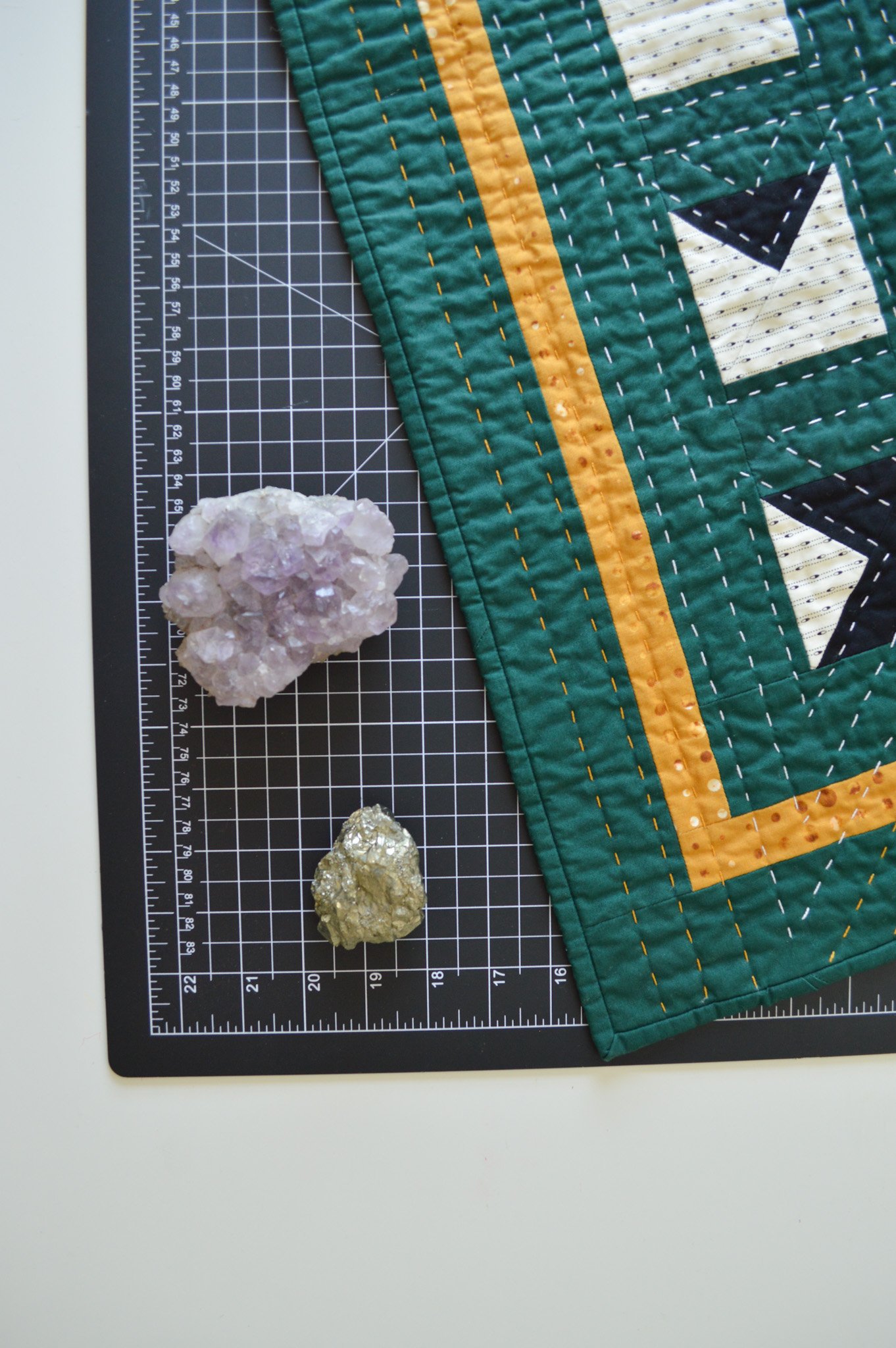  close up of a green mini quilt on a black cutting mat next to amethyst and pyrite stones 