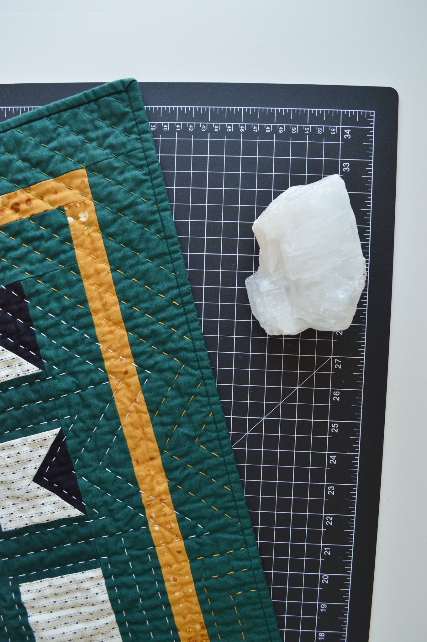  detail of a hand quilted mini quilt on a black cutting mat with calcite crystal 