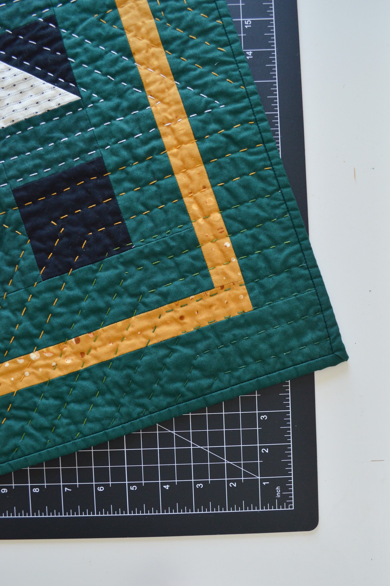 close up of a green, and-quilted mini quilt with colorful hand stitching 