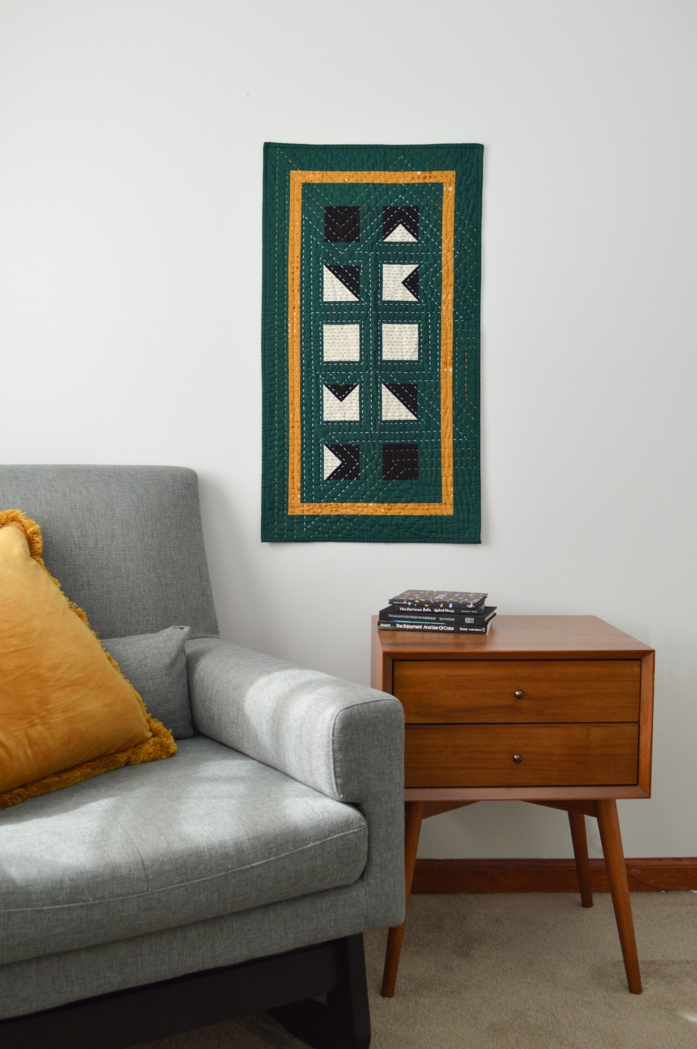  a green. hand quilted mini quilt hanging on a wall in a modern sitting corner 