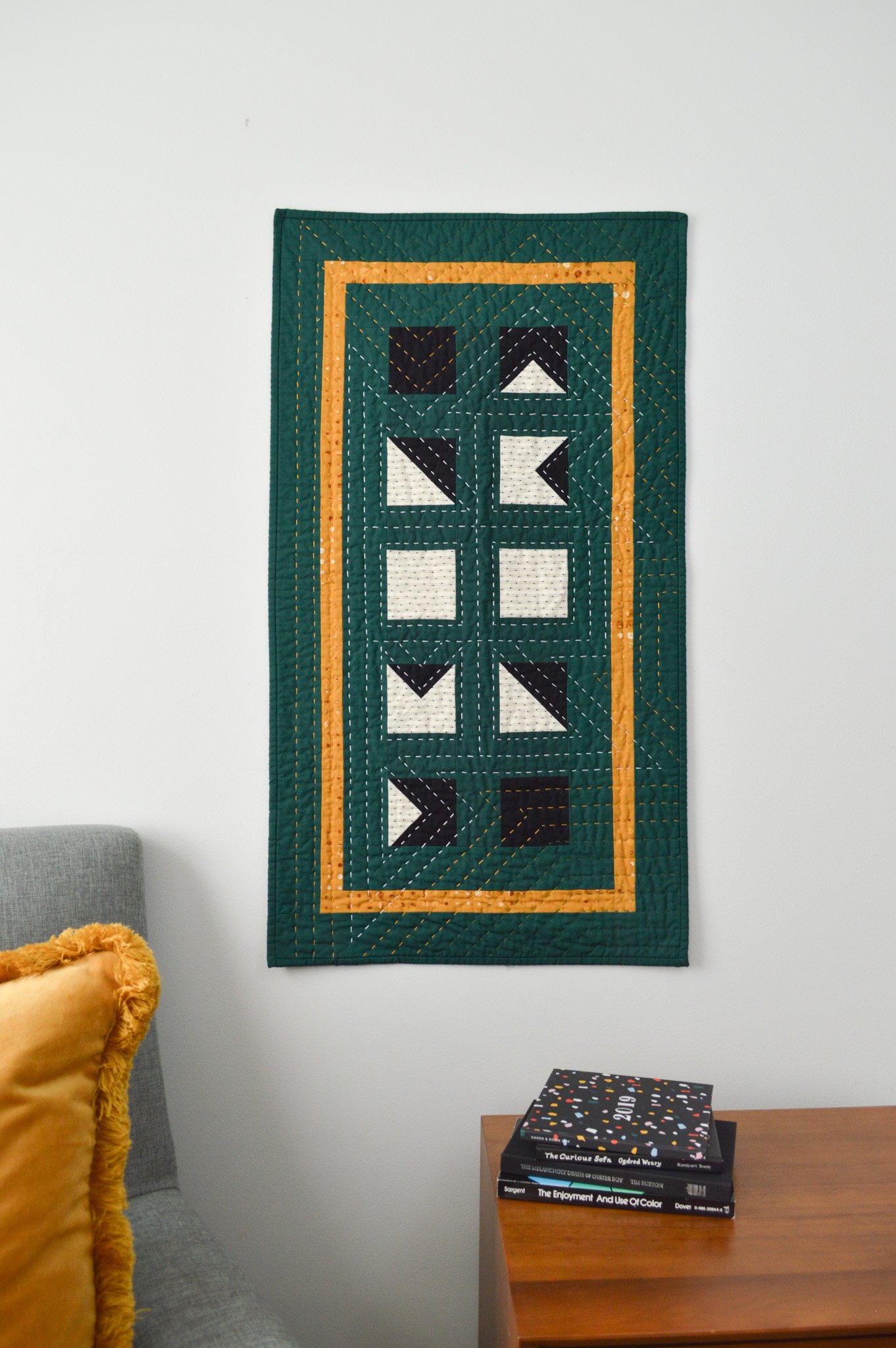  a hand quilted, green mini quilt hanging on a wall in a modern style room 