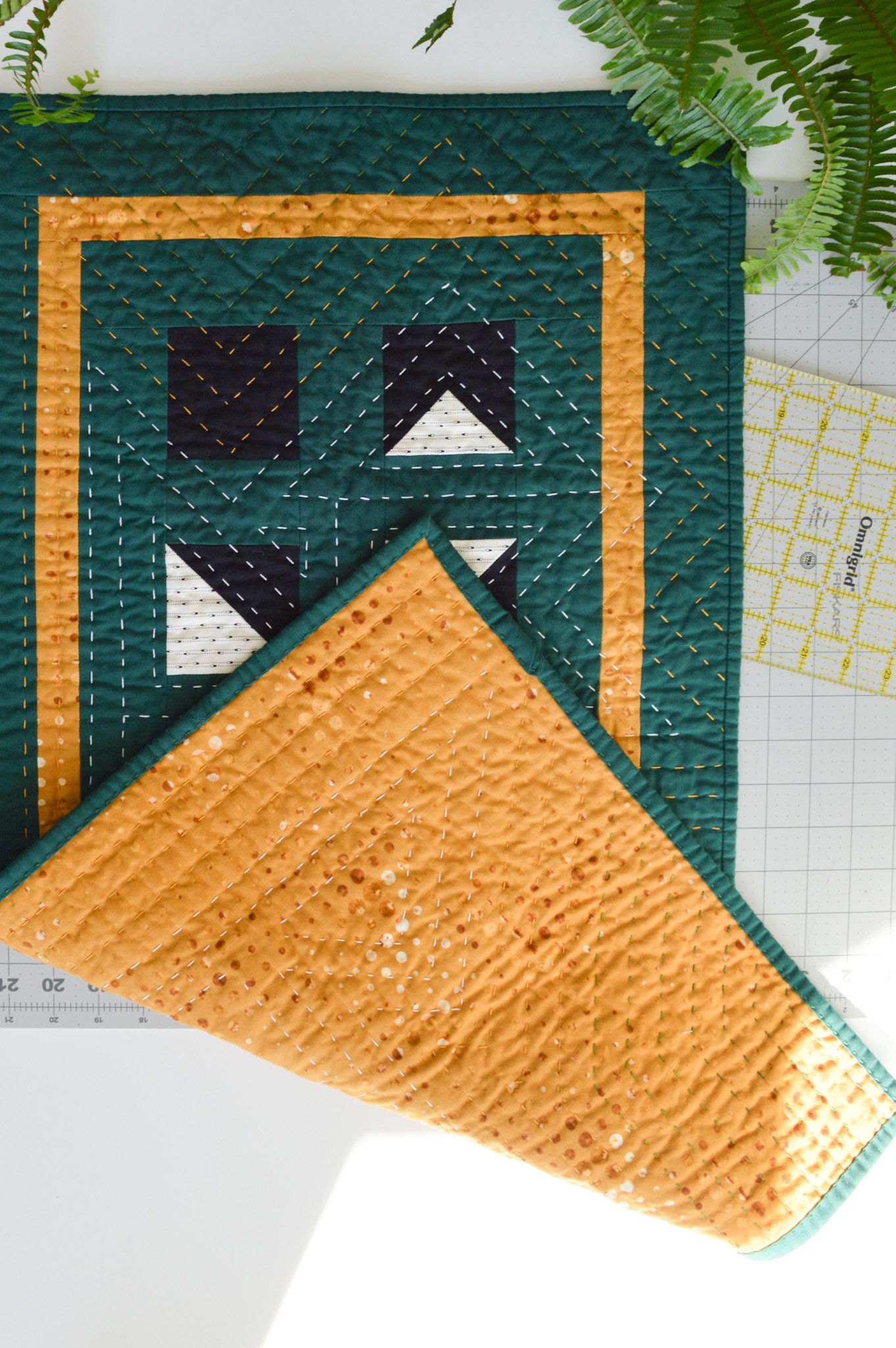  a hand quilted mini quilt on a cutting mat, folded to see both the front and back of the mini quilt at once 