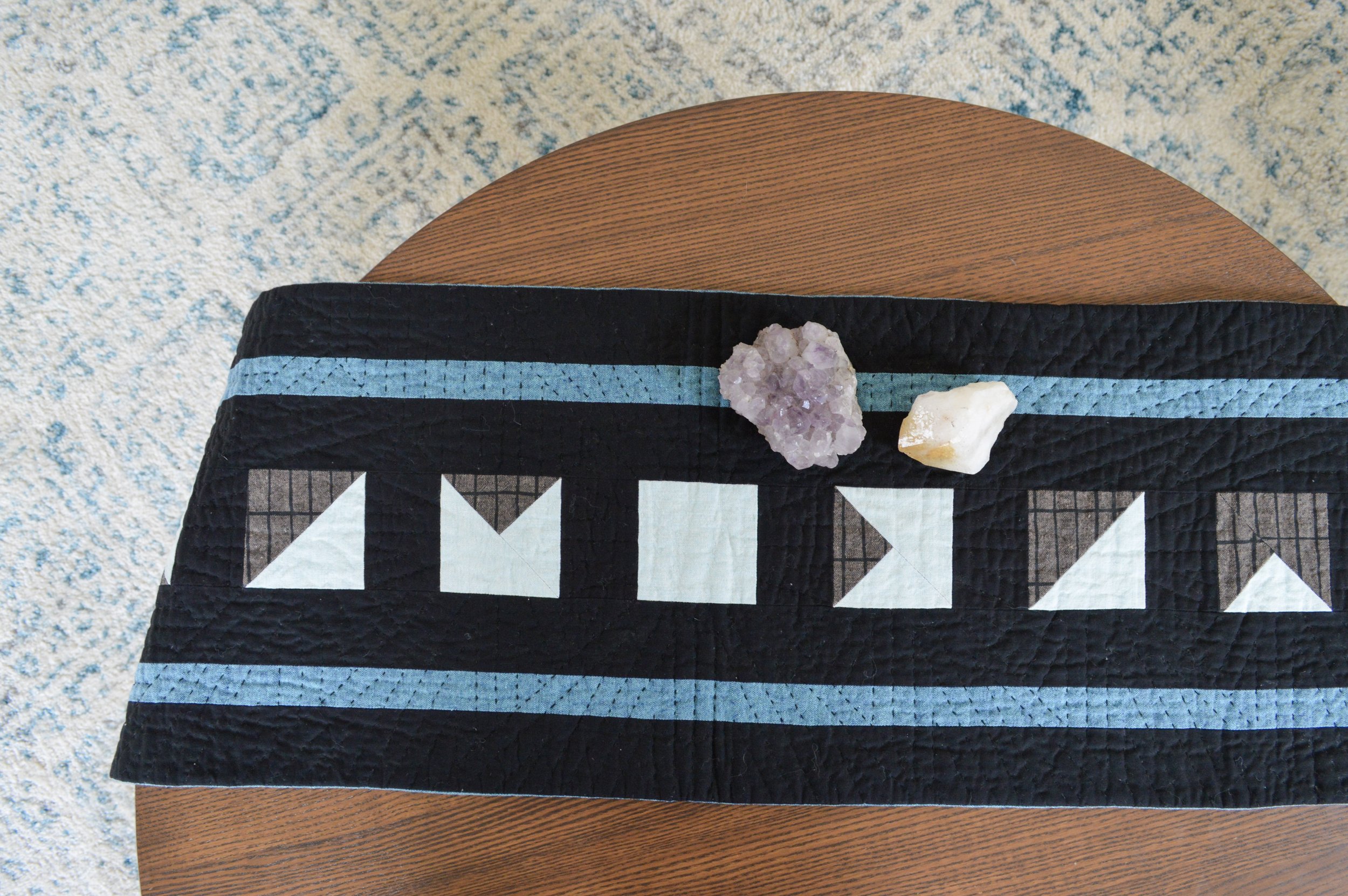  a black, hand quilted table runner on a wooden table with crystals 