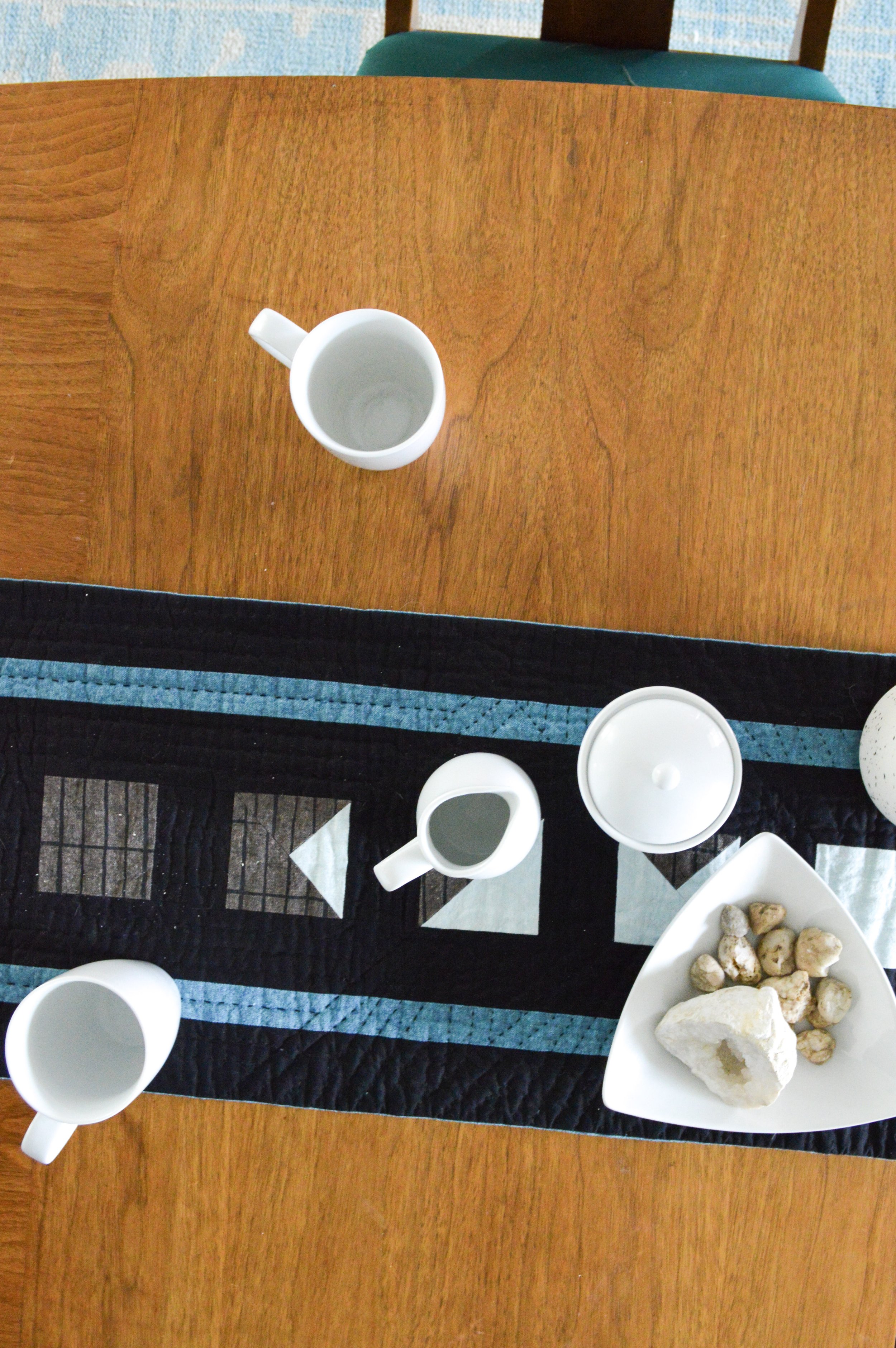  a hand quilted table runner on a table with setting for tea 