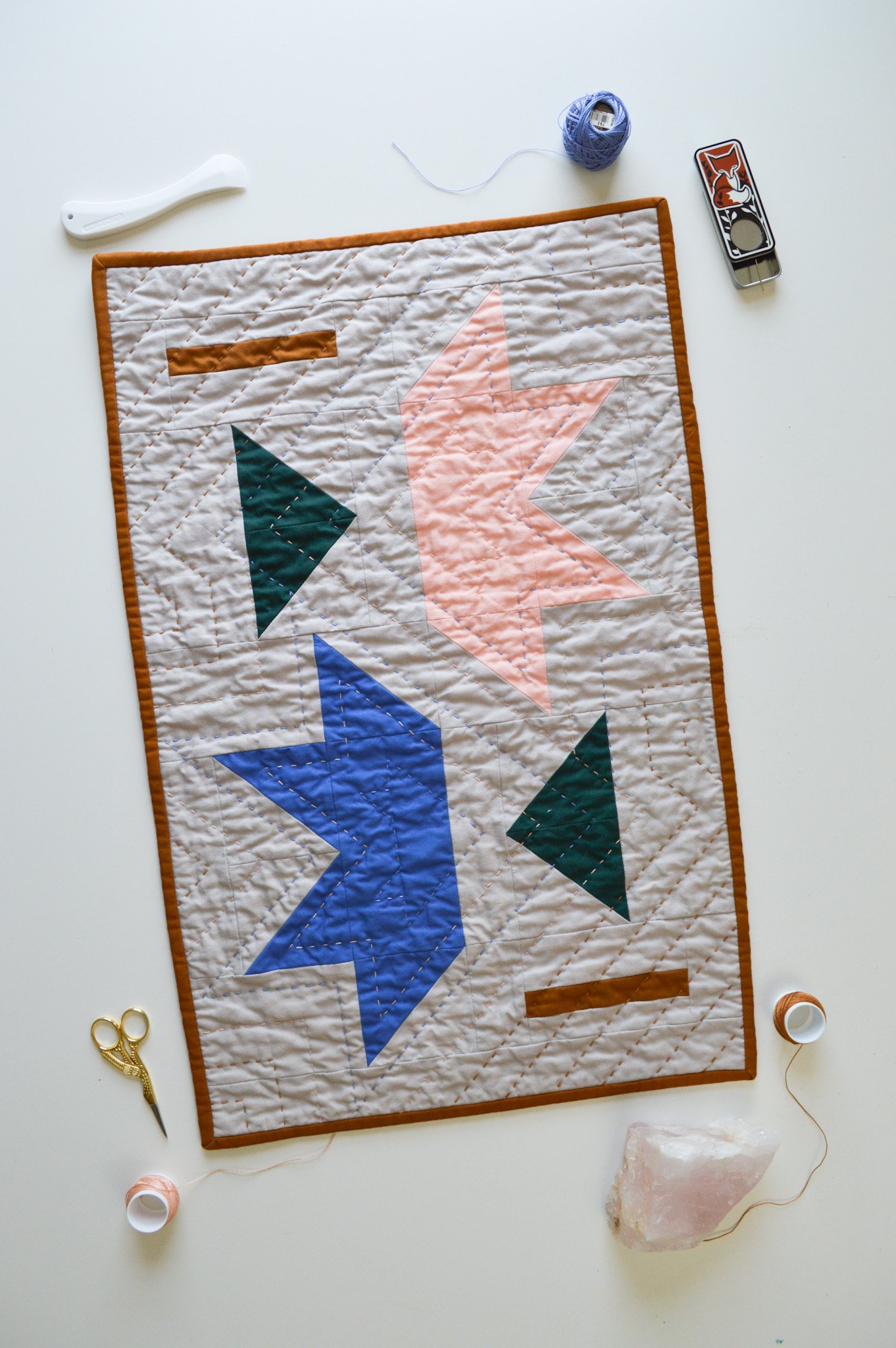  a hand-quilted mini quilt with two half stars surrounded by quilting notions and rose quartz 