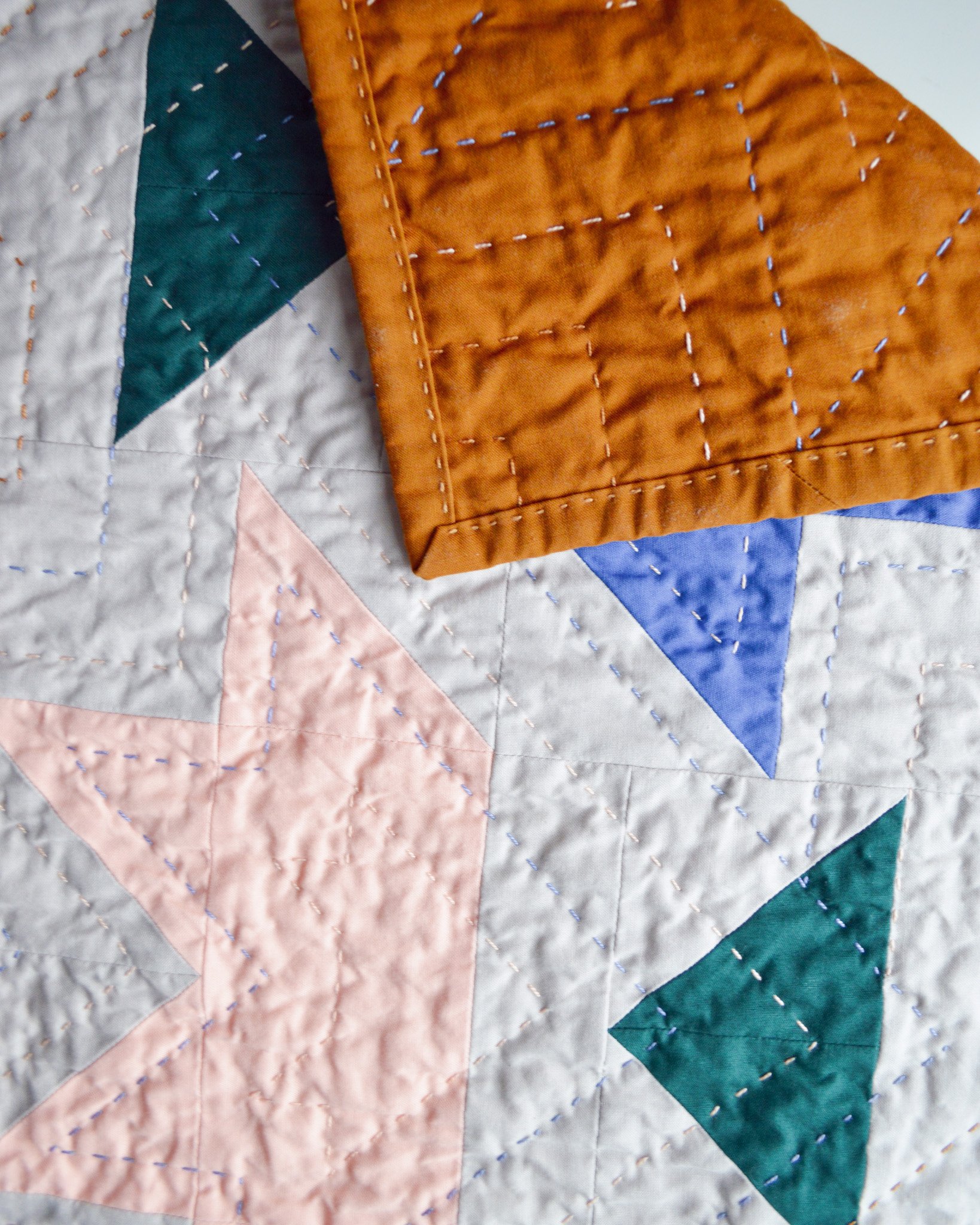 detail of a hand-quilted mini quilt, it's folded to see both the front and the back of the mini quilt 