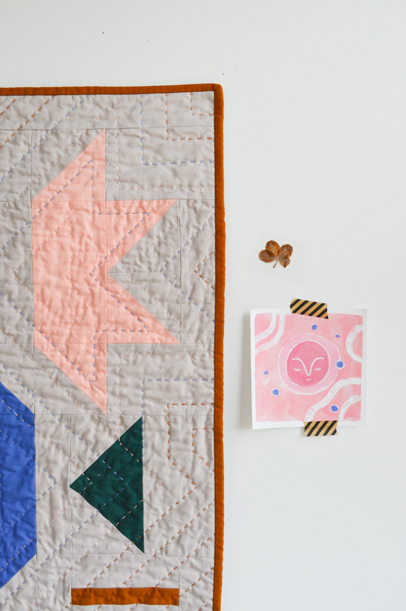  a hand-quilted wall hanging next to a small, pink drawing of the moon 