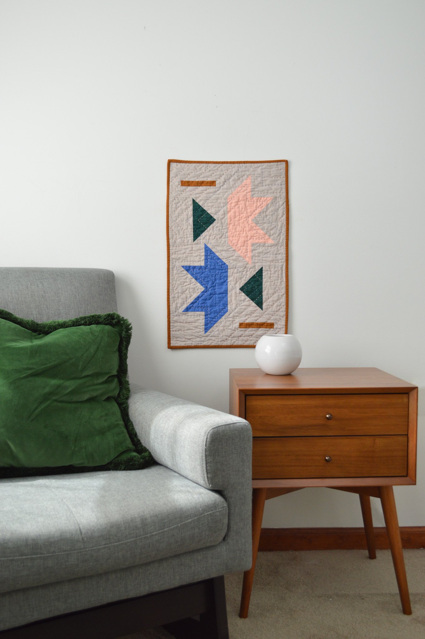  a modern mini quilt hanging on a wall amongst modern decor 