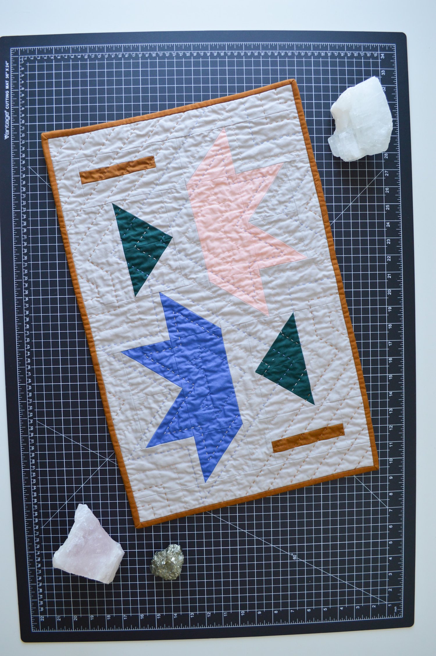  a modern mini quilt, hand-quilted, on a black cutting mat with stones and crystals 