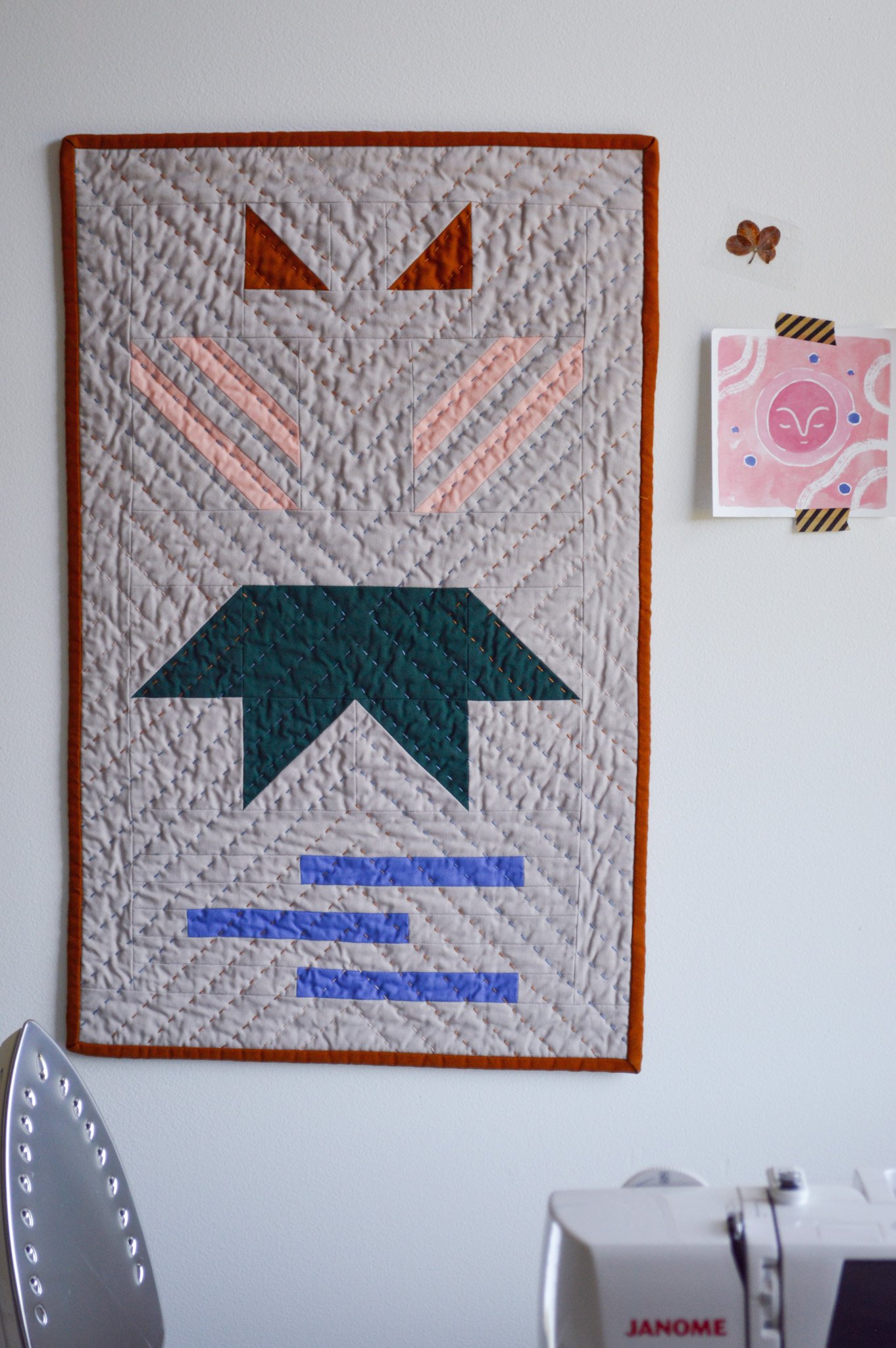  a modern mini quilt that is hand quilted hanging on the wall of a sewing studio 