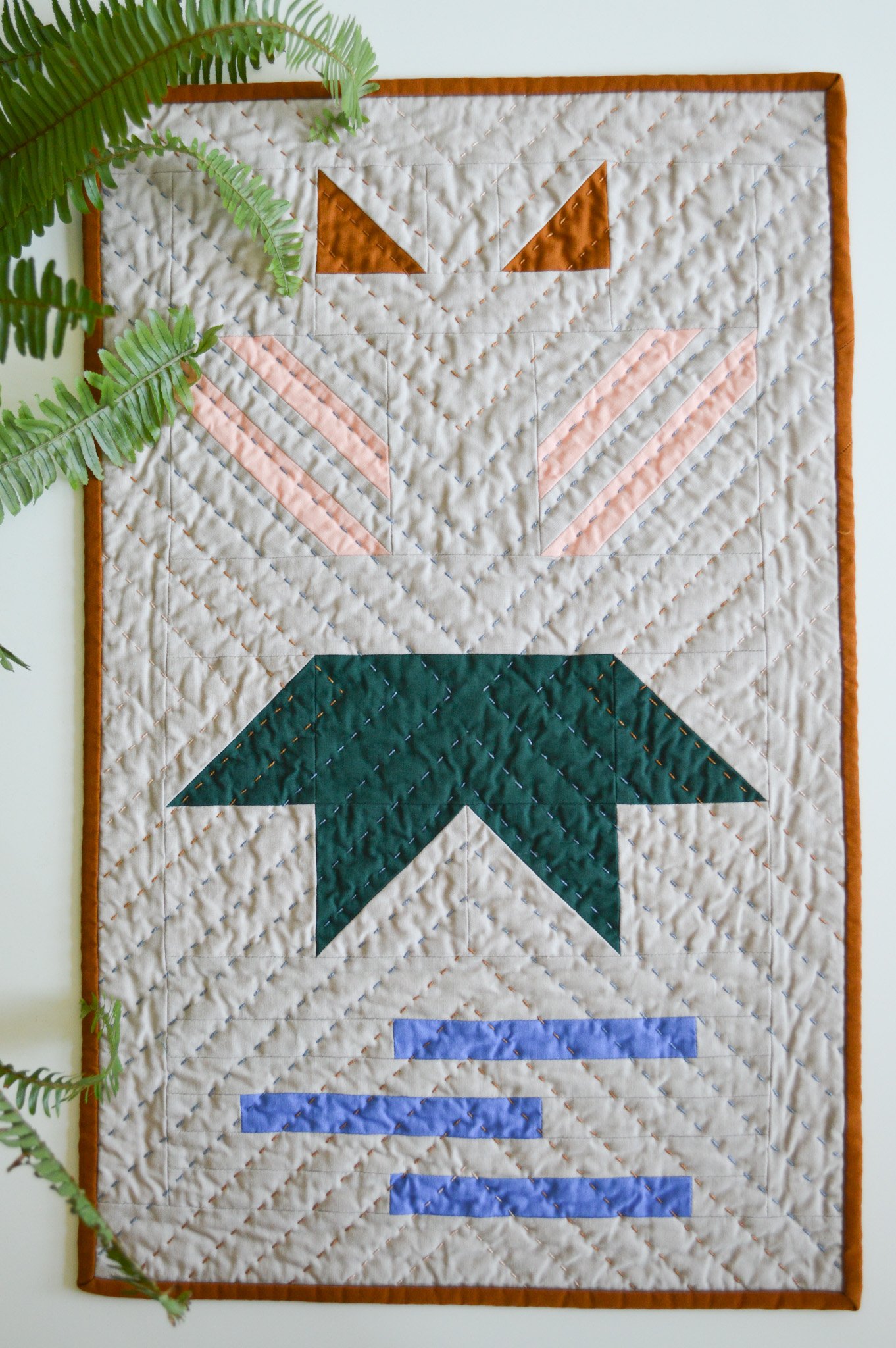  a modern mini quilt on a white table with fern leaves 