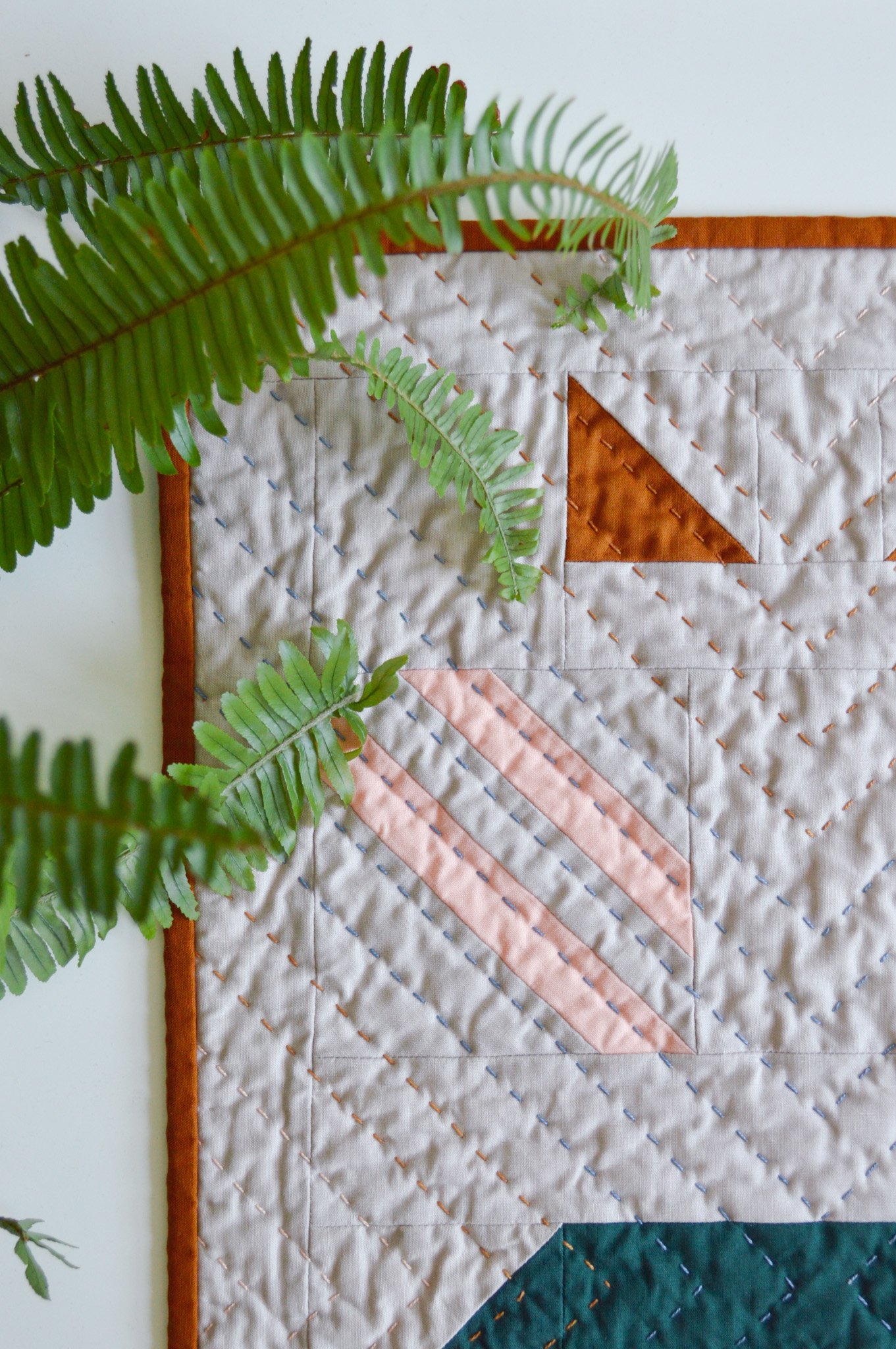  detail of a hand quilted mini quilt on a white table with fern leaves 