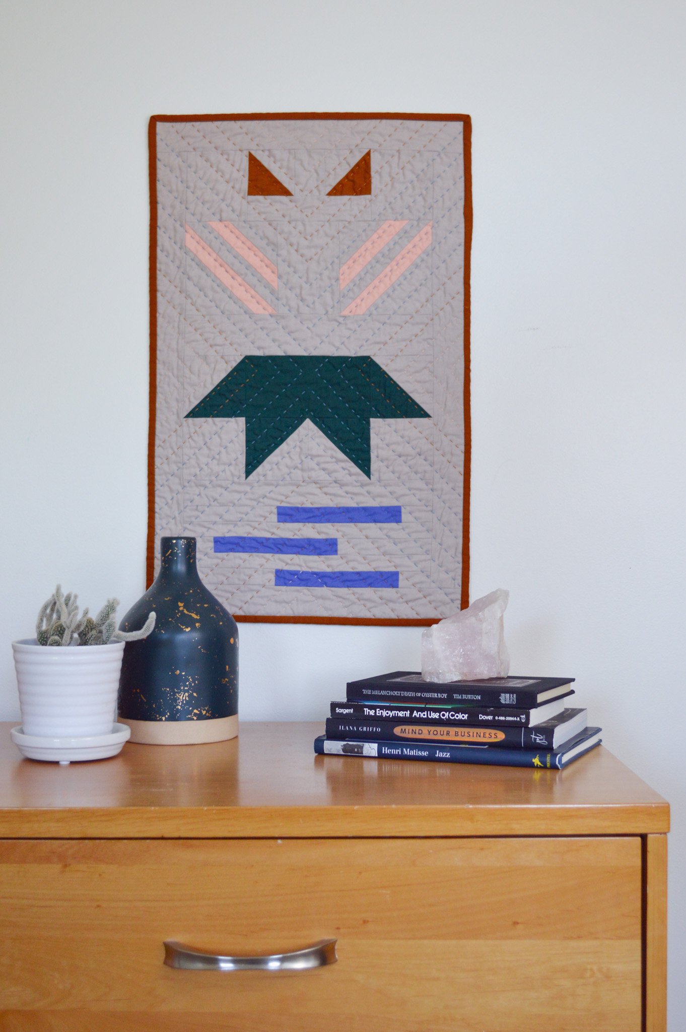  a modern, quilted wall hanging on a white wall with modern decor 
