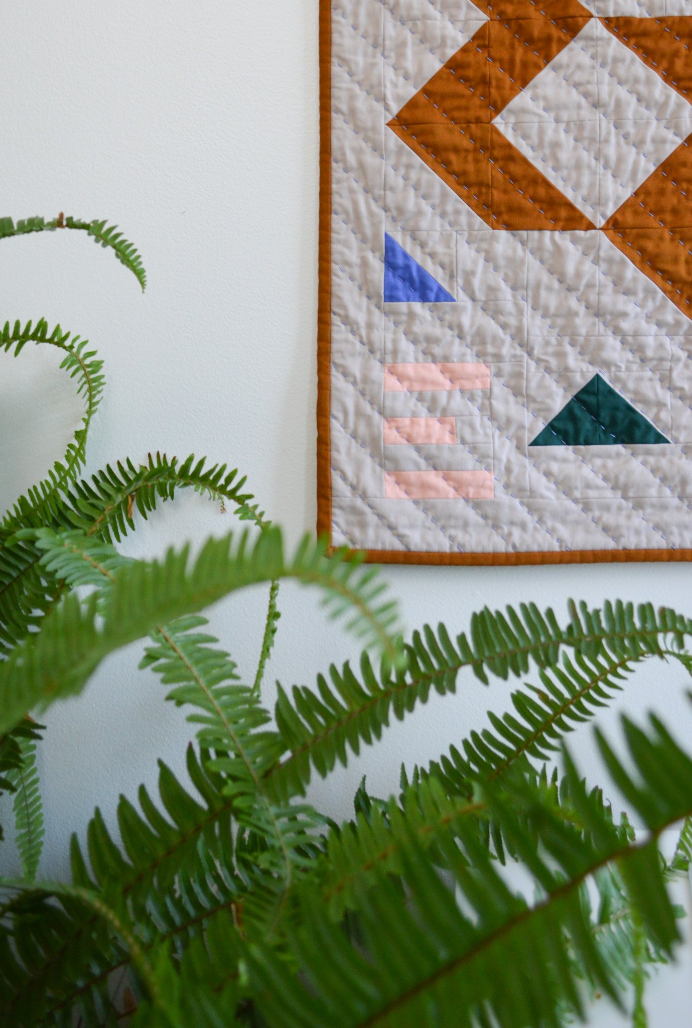  modern mini quilt handing above a green fern 