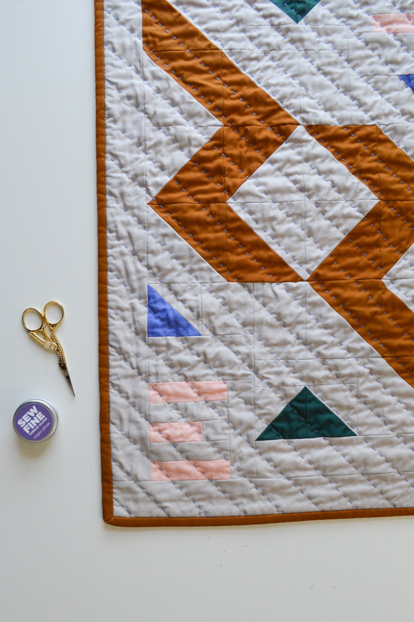  a modern mini quilt on a white table with gold scissors and thread gloss 